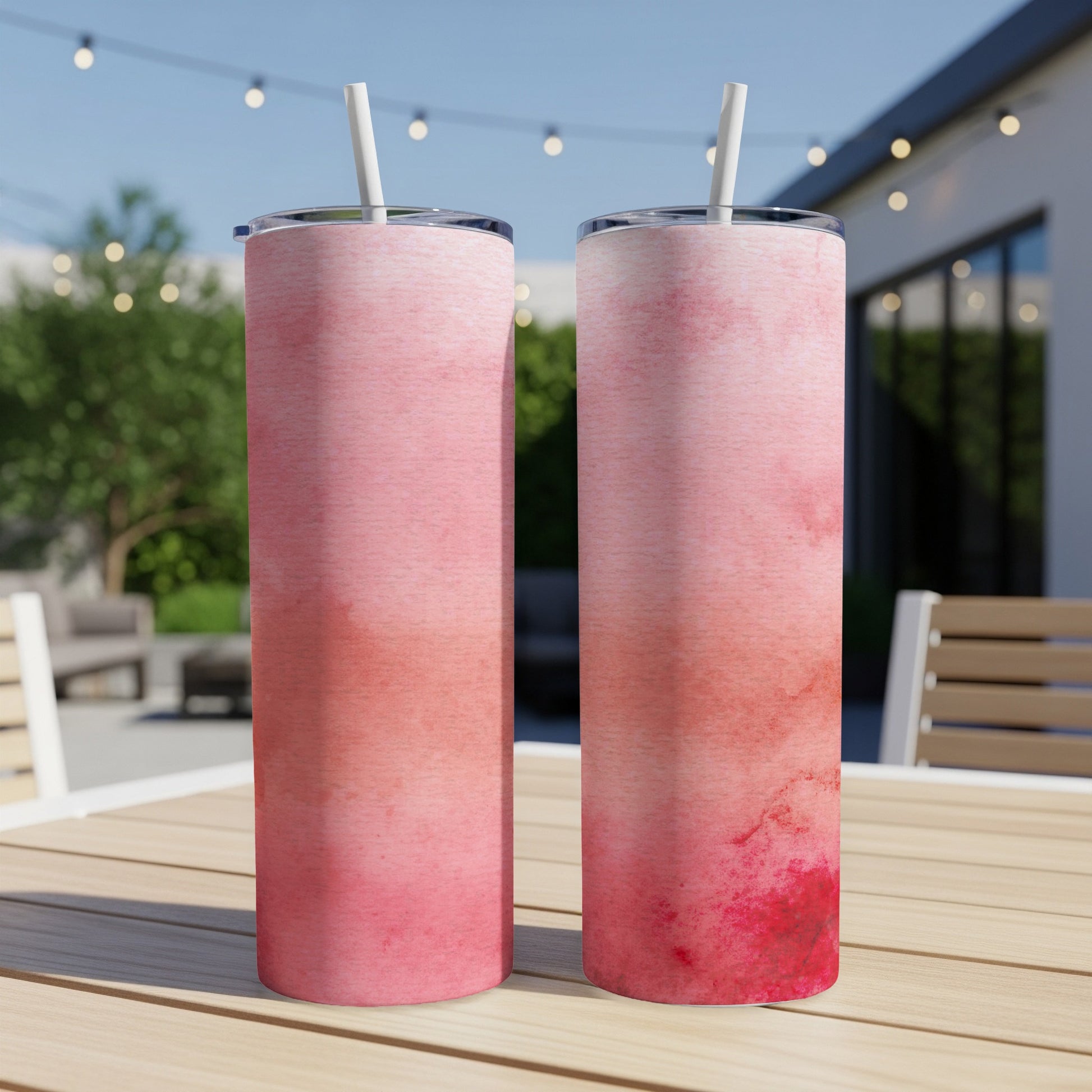 Two pink watercolor tumblers with straws on a wooden table.