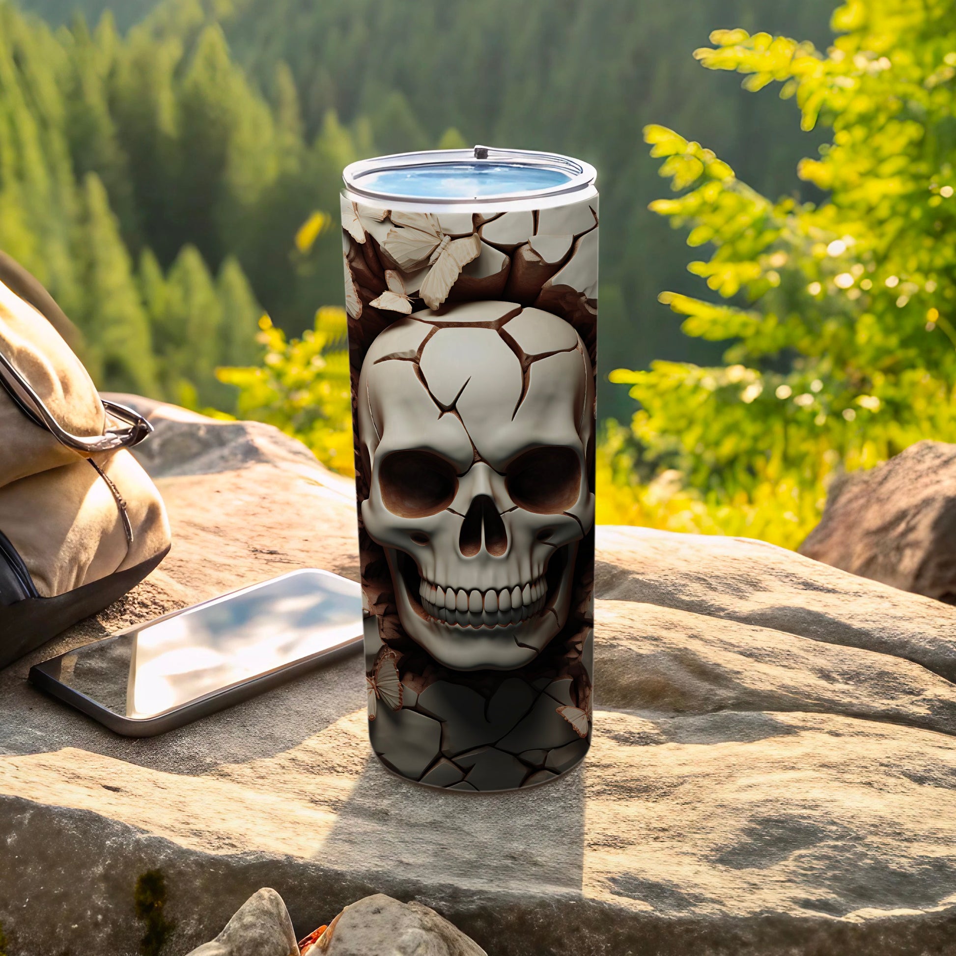 Cracked skull design on a tumbler, resting on rocks with a backpack and phone.