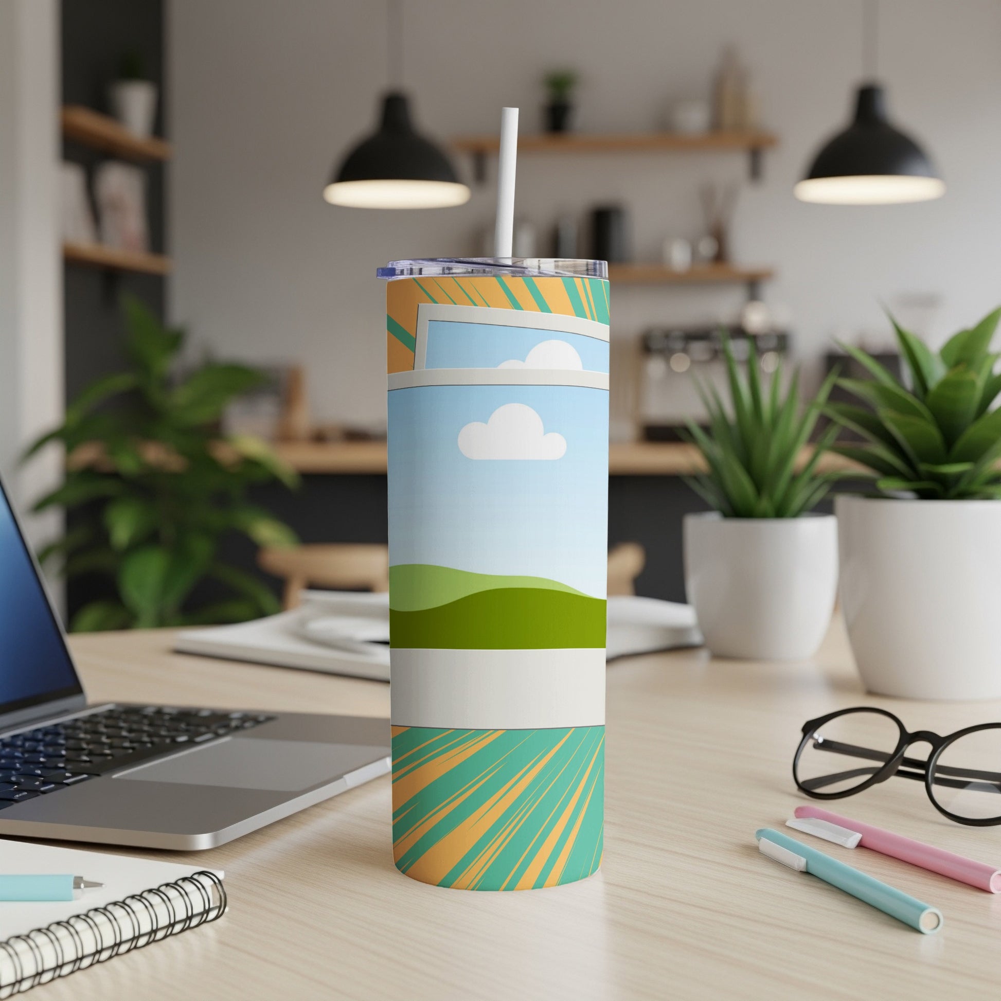 Tall tumbler with landscape design, straw, and a desk setting.
