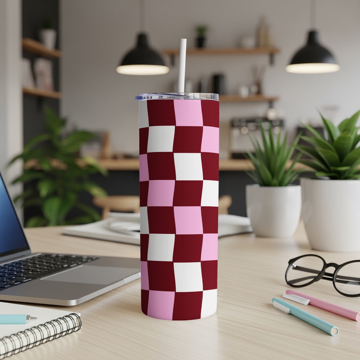 Pink and burgundy checkered tumbler with straw on a desk.