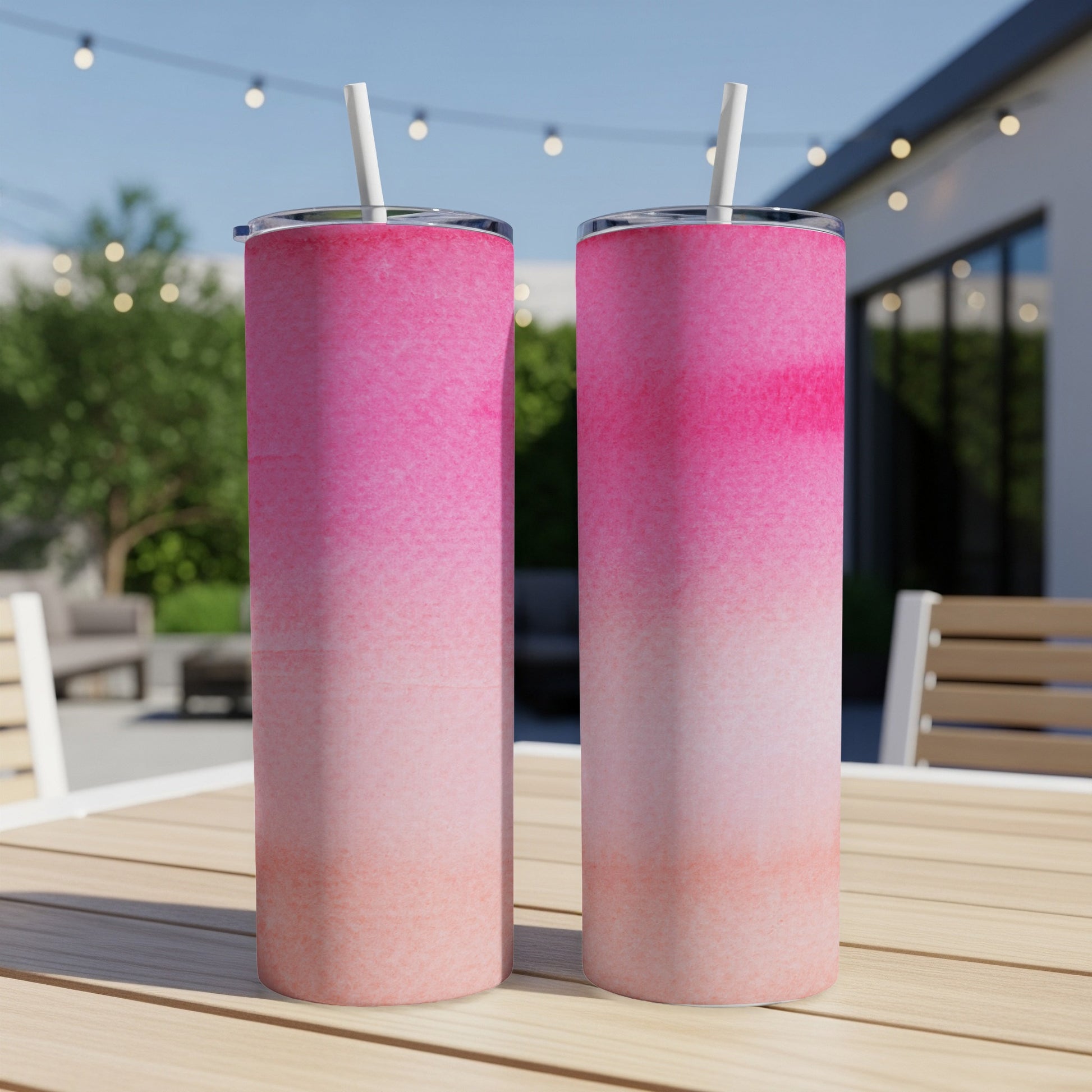 Two pink gradient tumblers with straws on a wooden table outdoors.