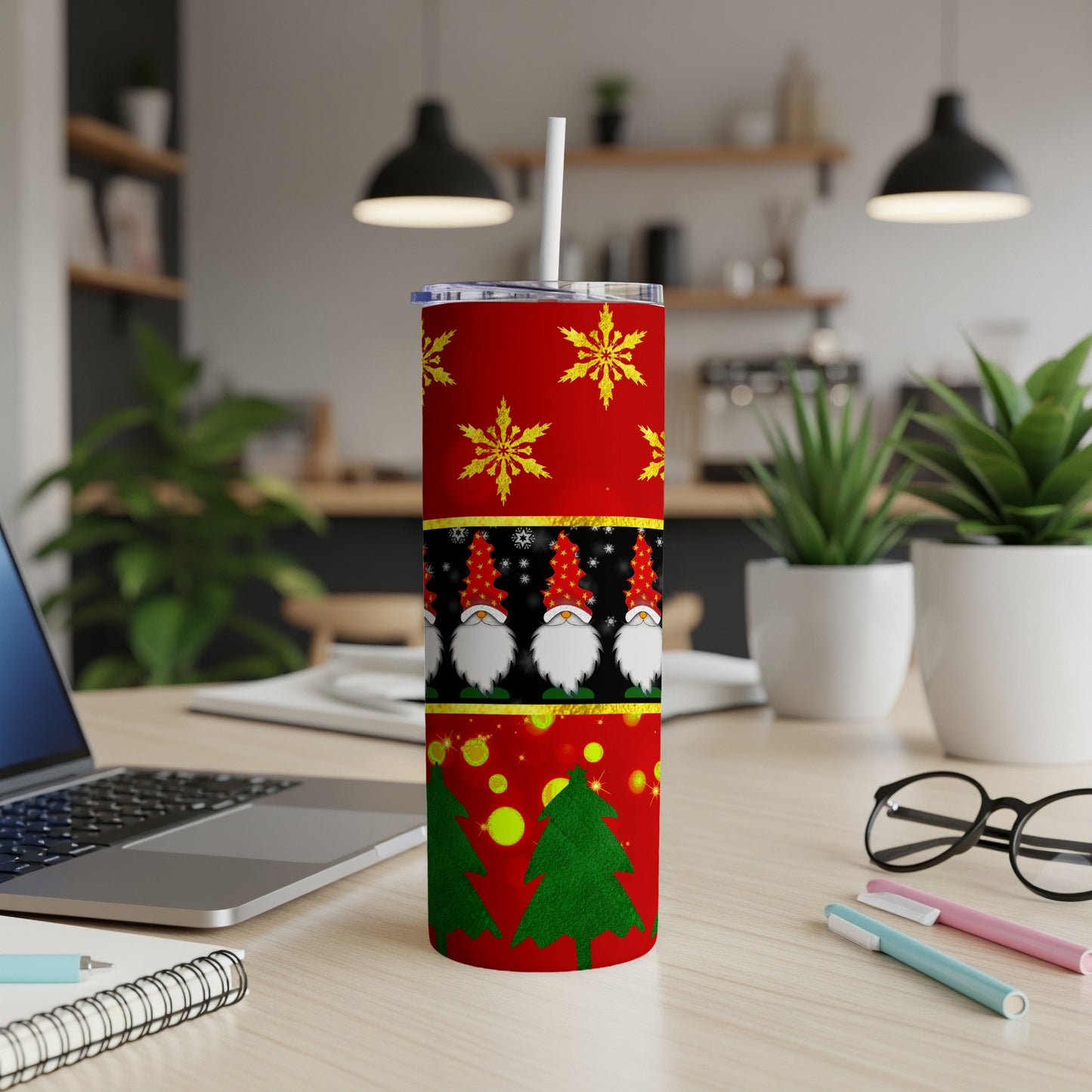 Red tumbler with gnomes, snowflakes, and Christmas trees, on a desk.