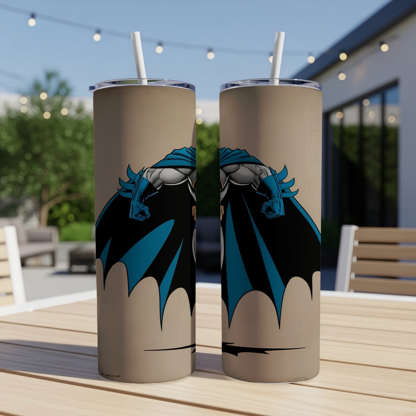 Two tan tumblers featuring Batman artwork, set on a table outdoors.