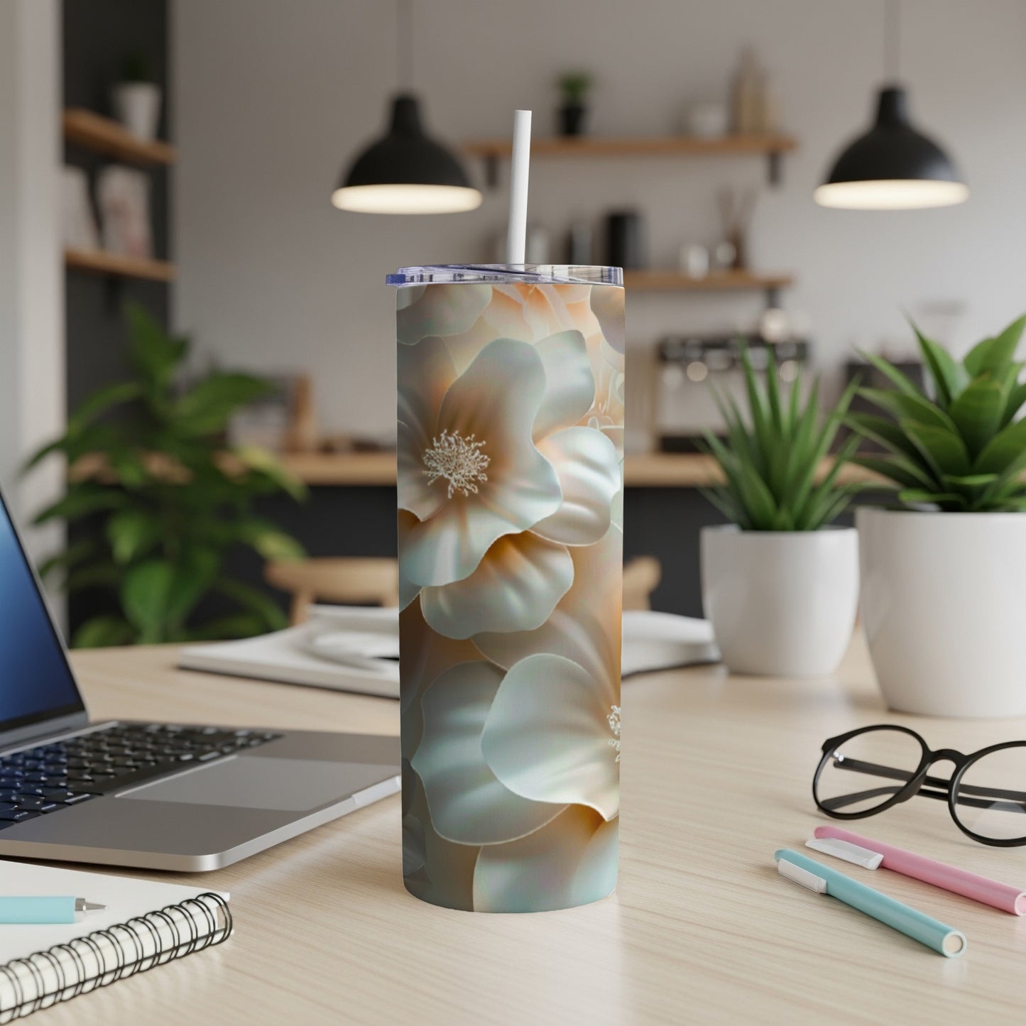 Floral tumbler with straw on a desk with a laptop and pens.