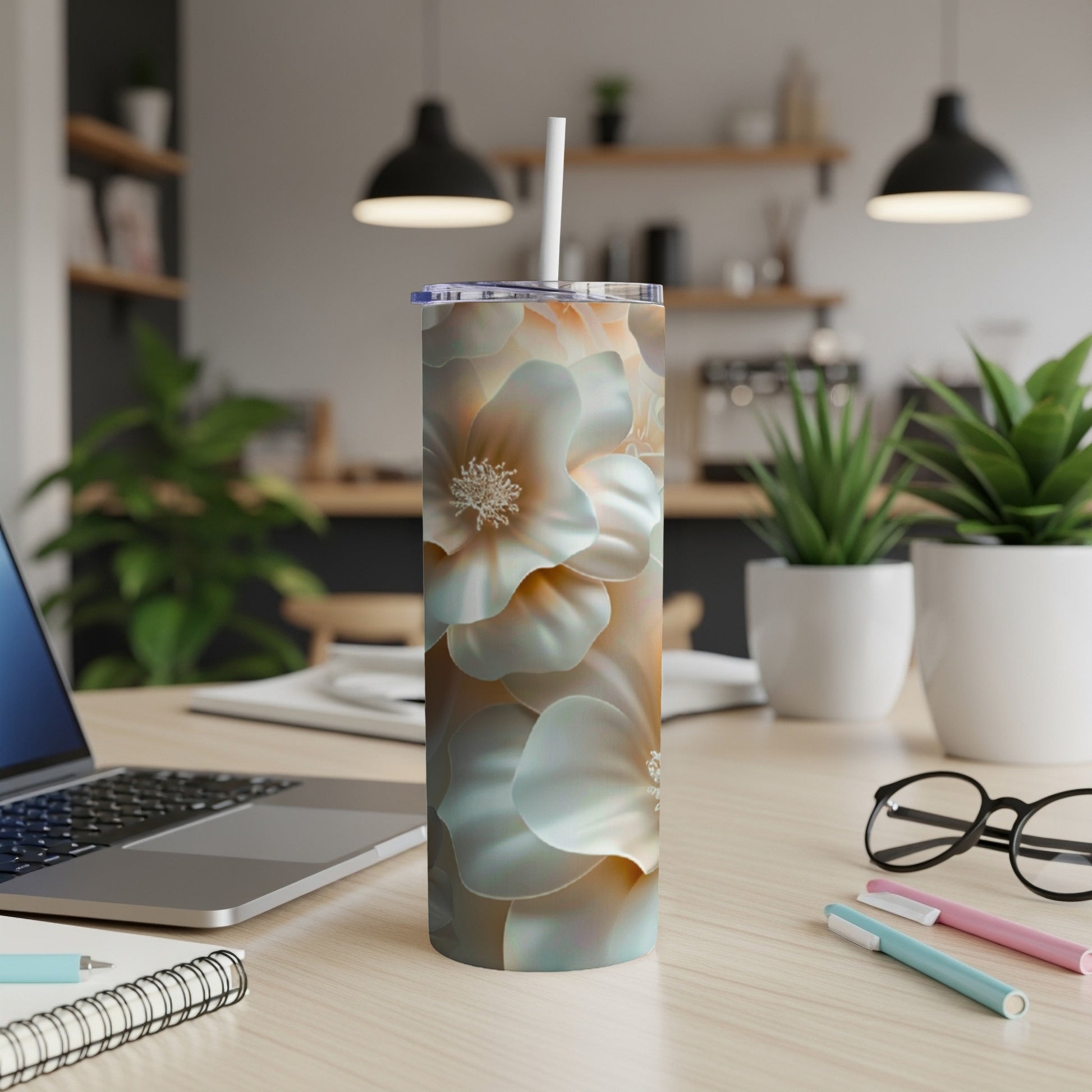 Floral tumbler with straw on a desk with a laptop and pens.