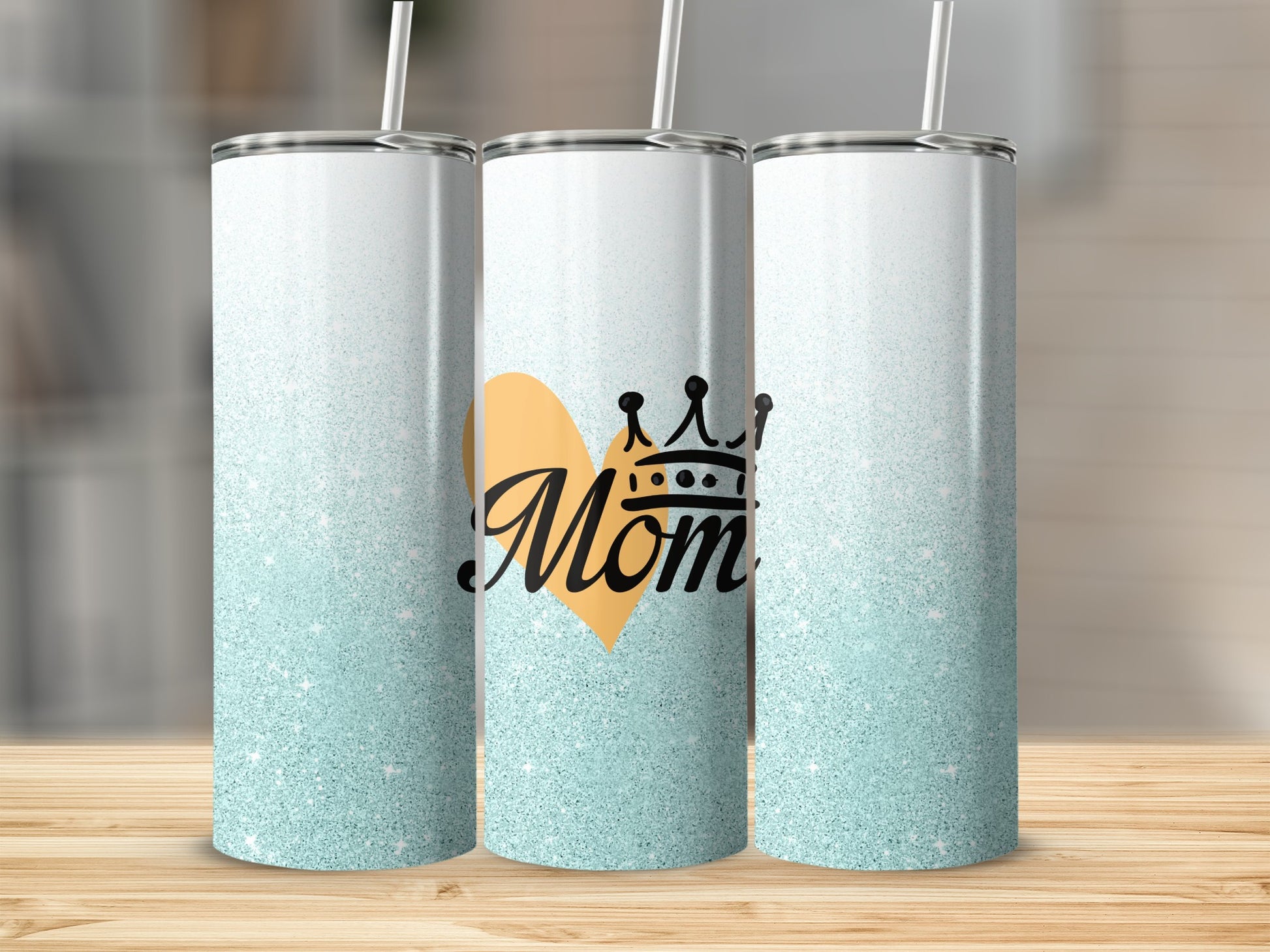 Three skinny tumblers with "Mom" and a heart with a crown, on a wooden surface.