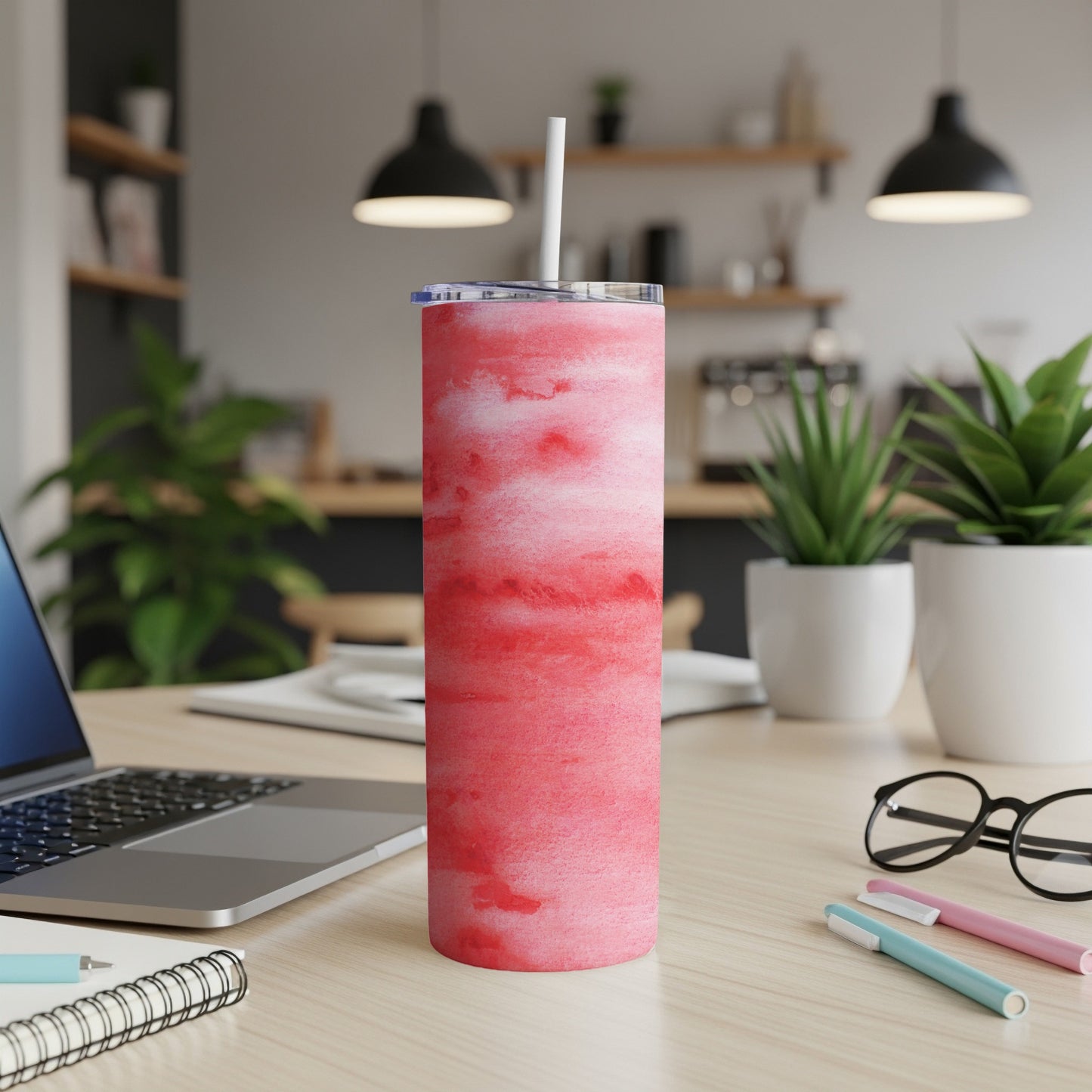 Pink watercolor tumbler with straw on a desk next to a laptop and pens.
