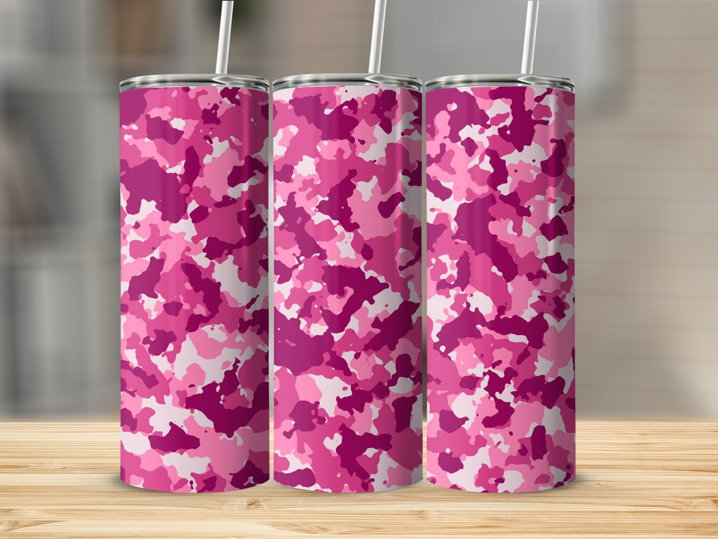 Three pink camouflage tumblers with white straws on a wooden surface.