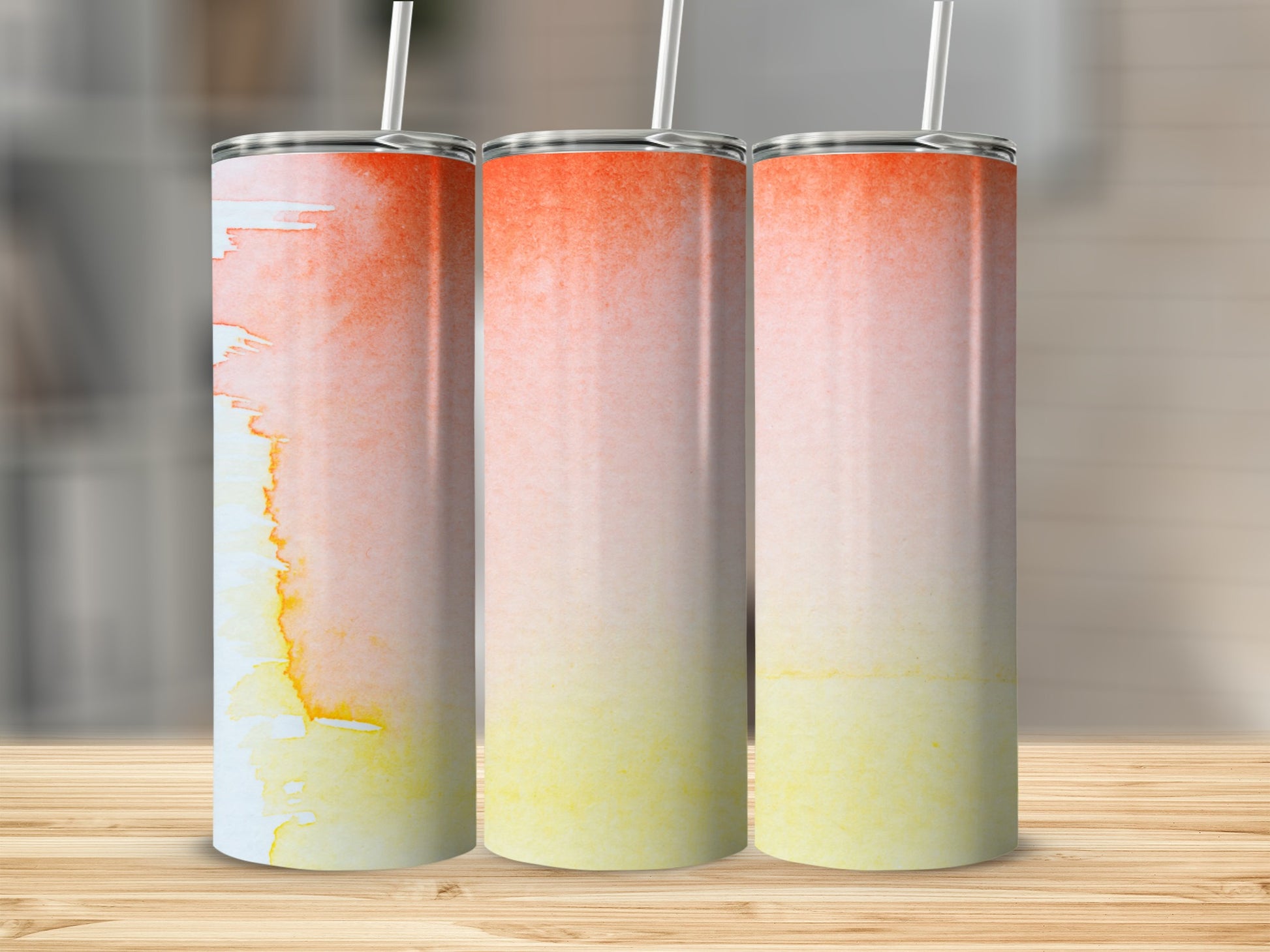 Three tumblers with orange to yellow watercolor design on a wooden surface.