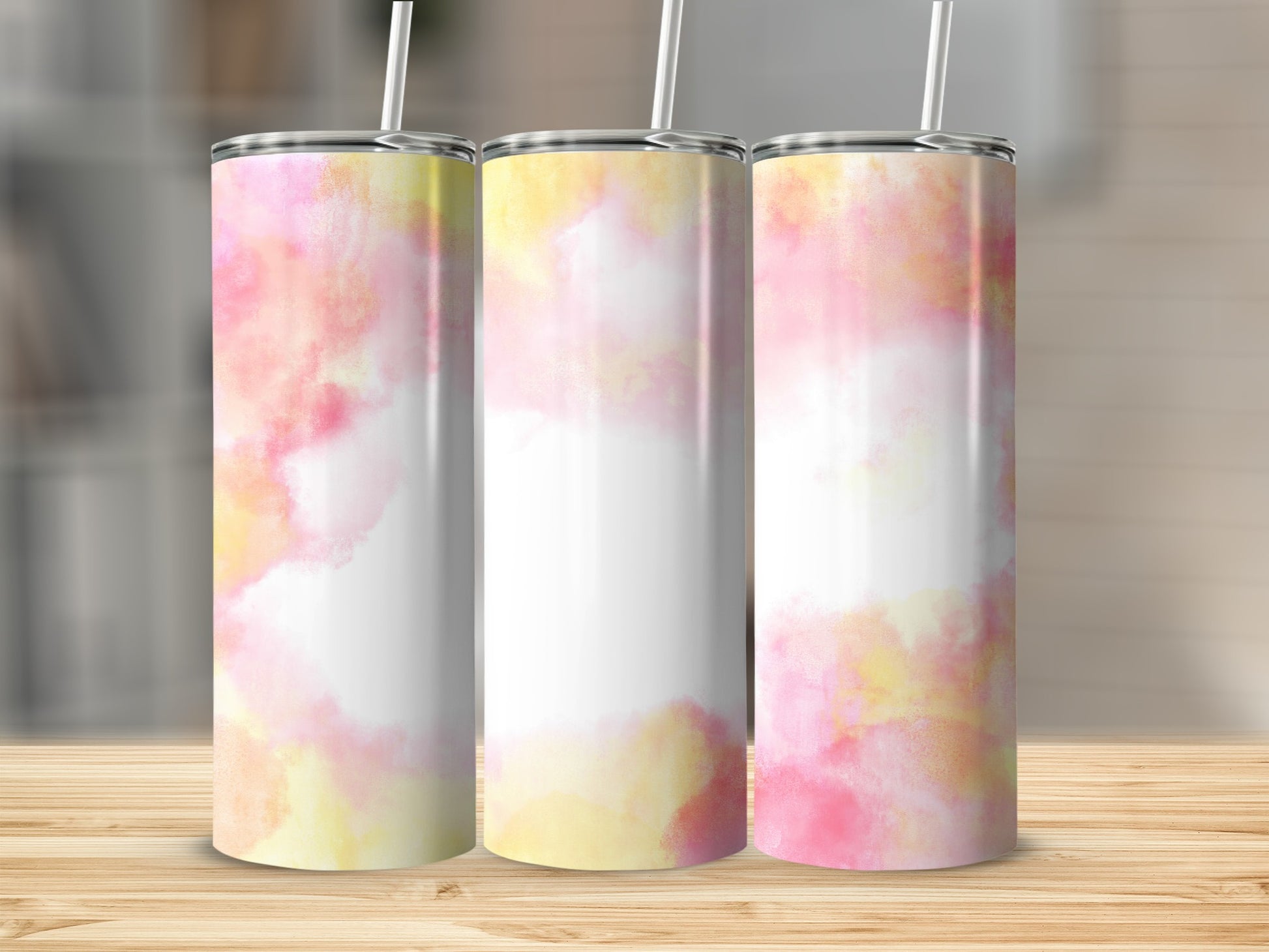 Three tumblers with a pink and yellow watercolor design on a wooden surface.