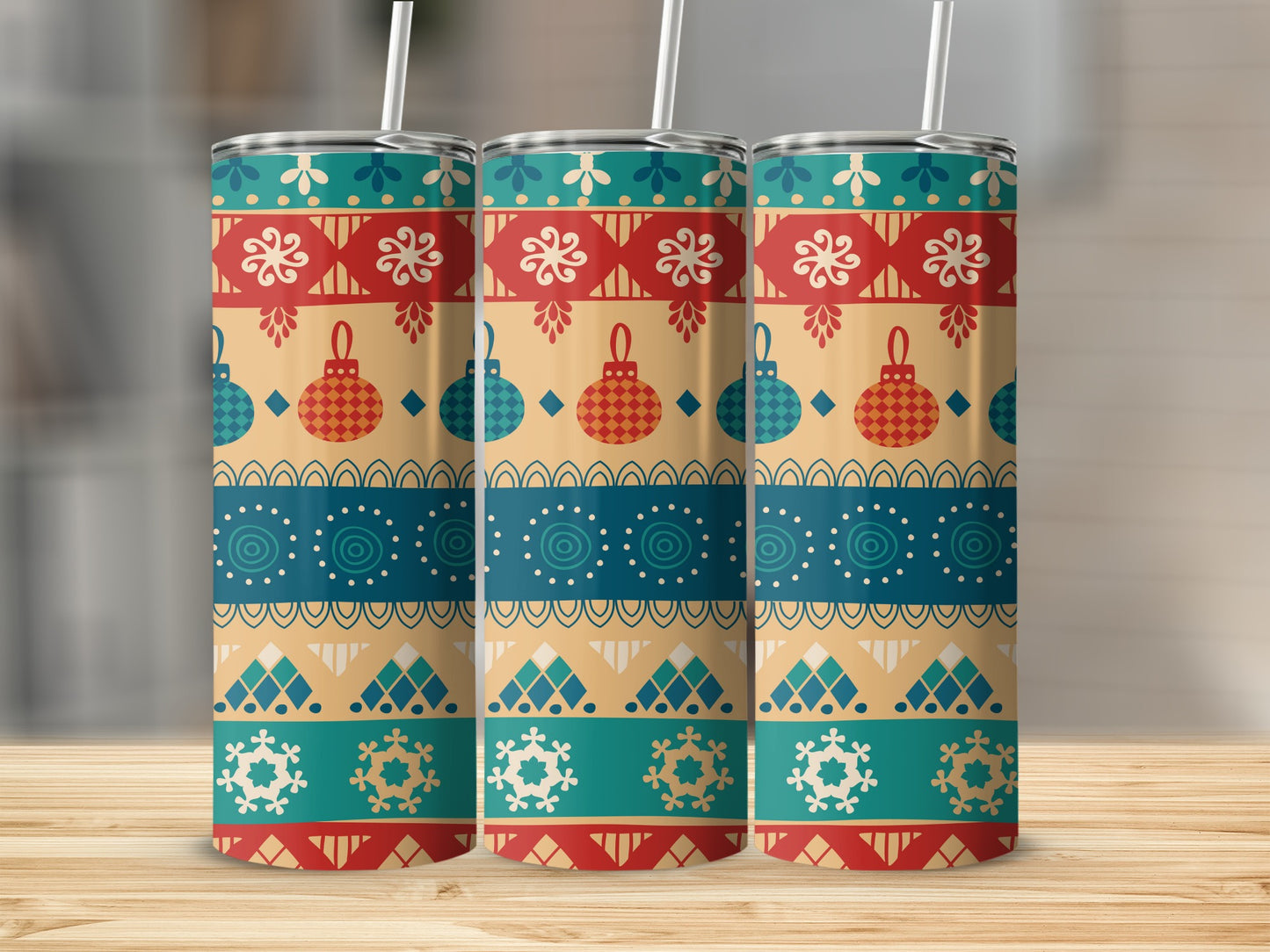 Three identical festive patterned tumblers with straws on a wooden surface.