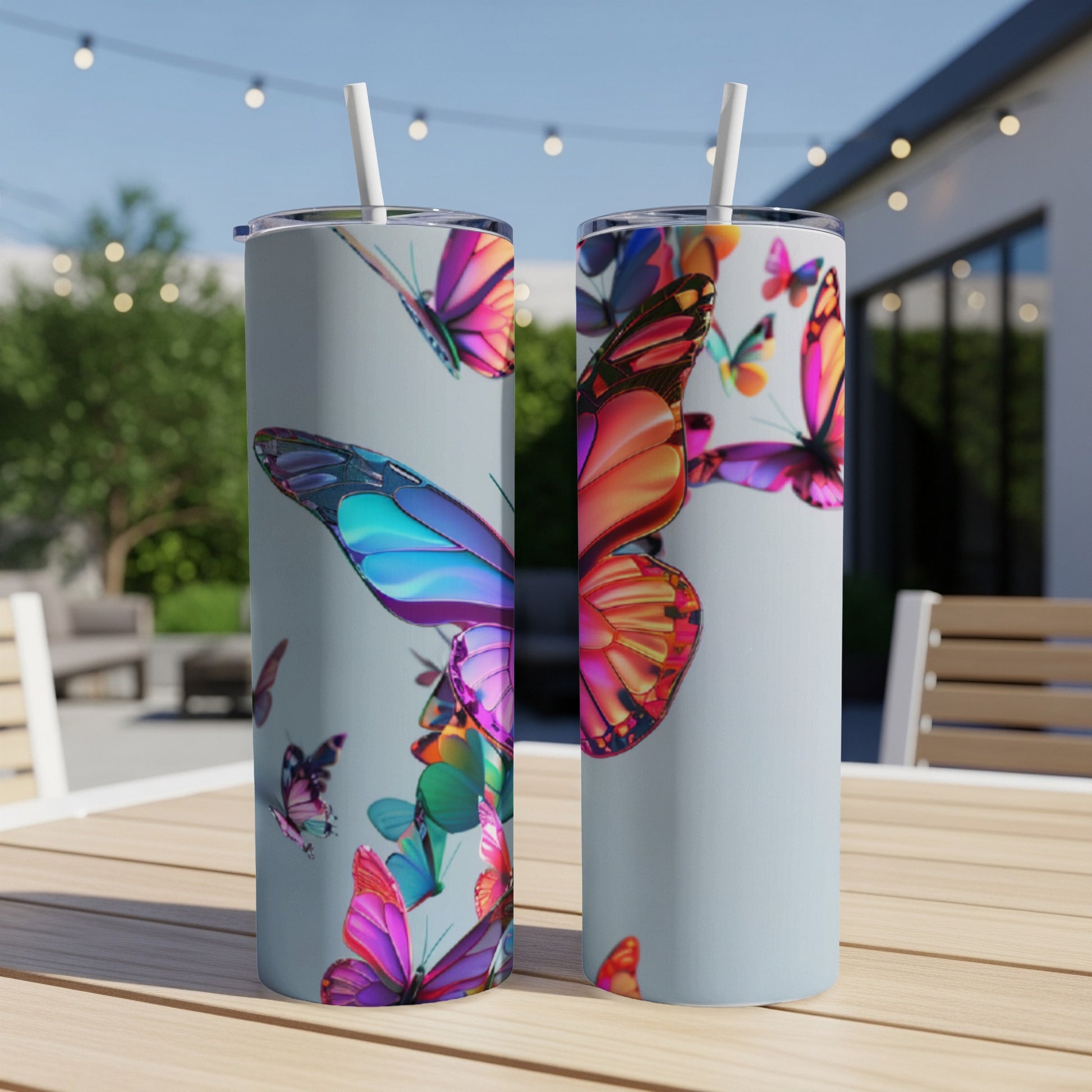 Two tumblers with colorful butterfly designs on a wooden table outdoors.