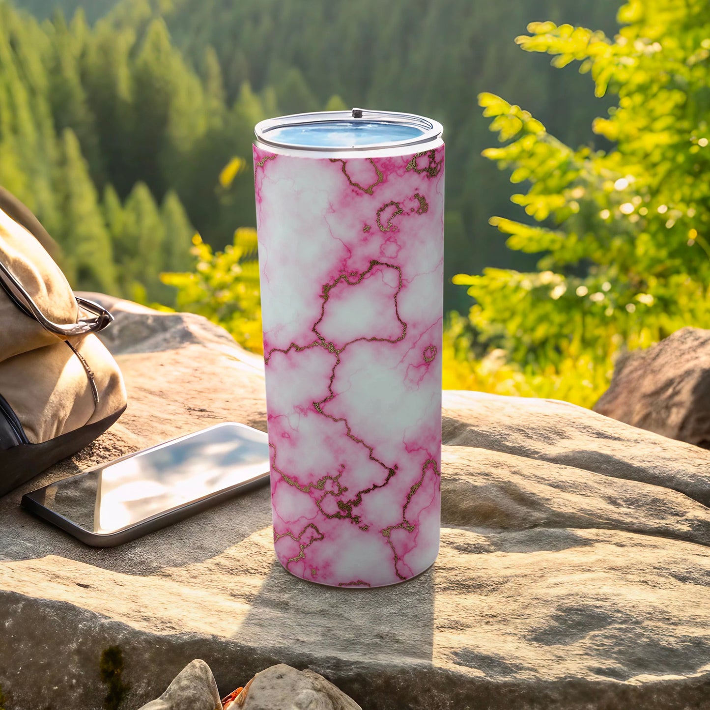 Pink marble tumbler with gold veining on a rock, phone, and backpack.