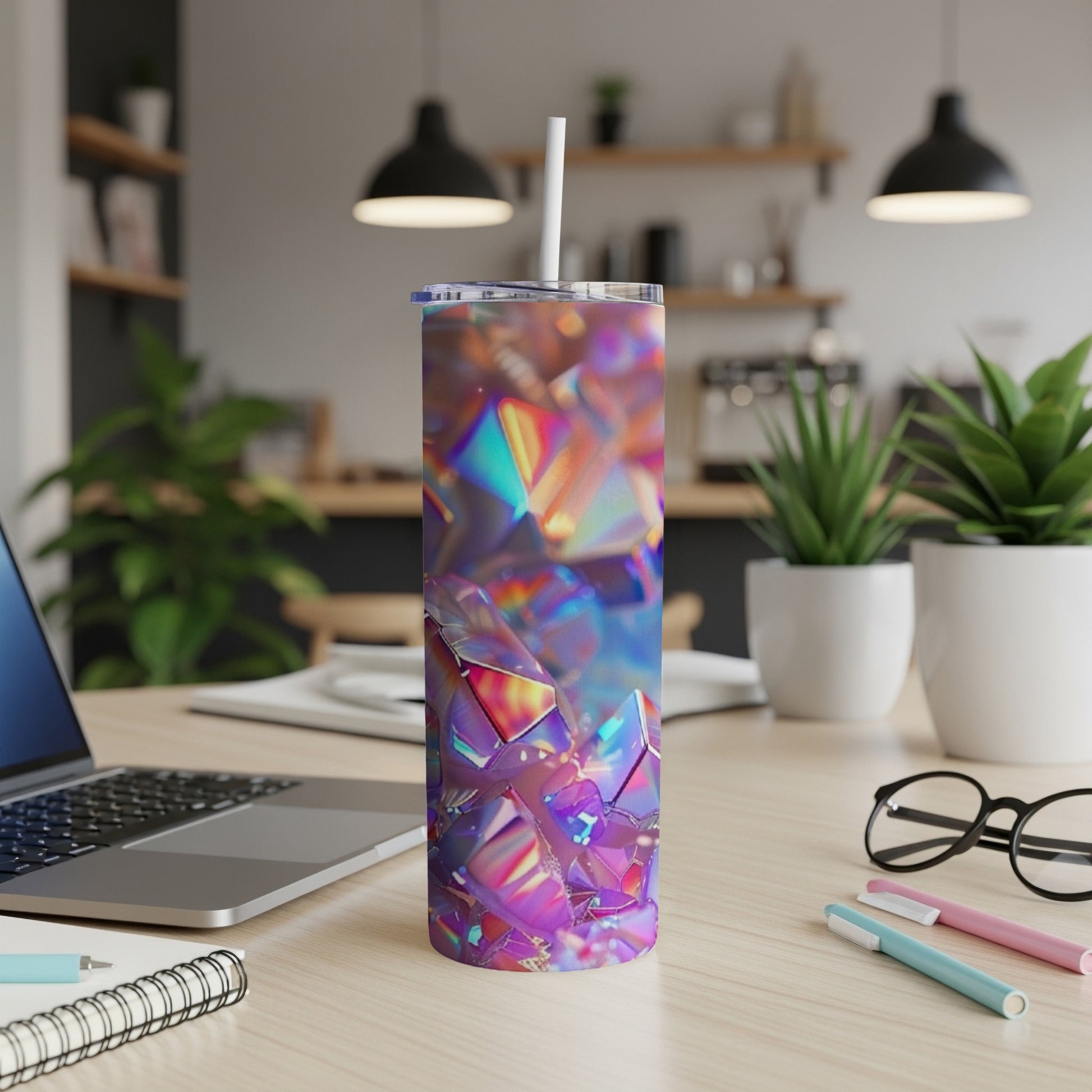Holographic geometric tumbler with straw on desk next to laptop.