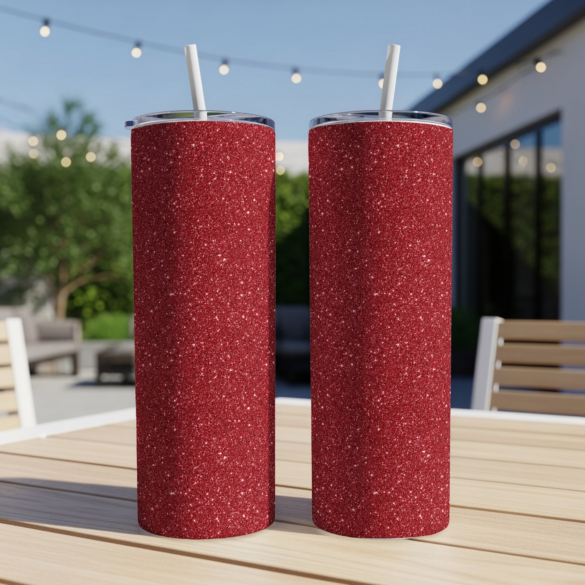 Two red glitter tumblers with white straws sit on a wooden table outdoors.