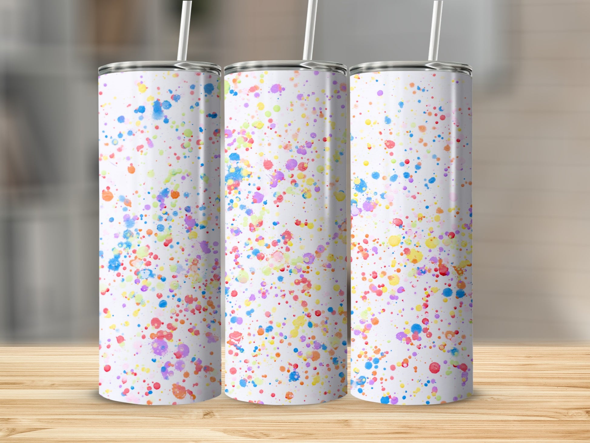 Three white tumblers with colorful paint splatter design on wooden surface.