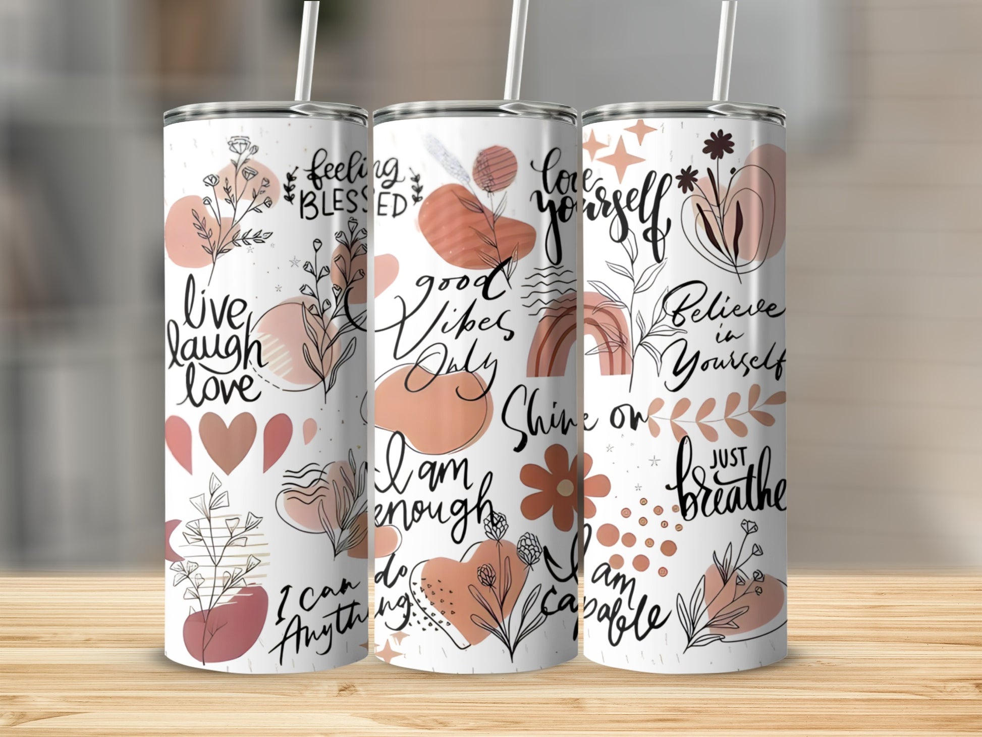 Three tumblers with inspirational text and floral line art on a wooden surface.