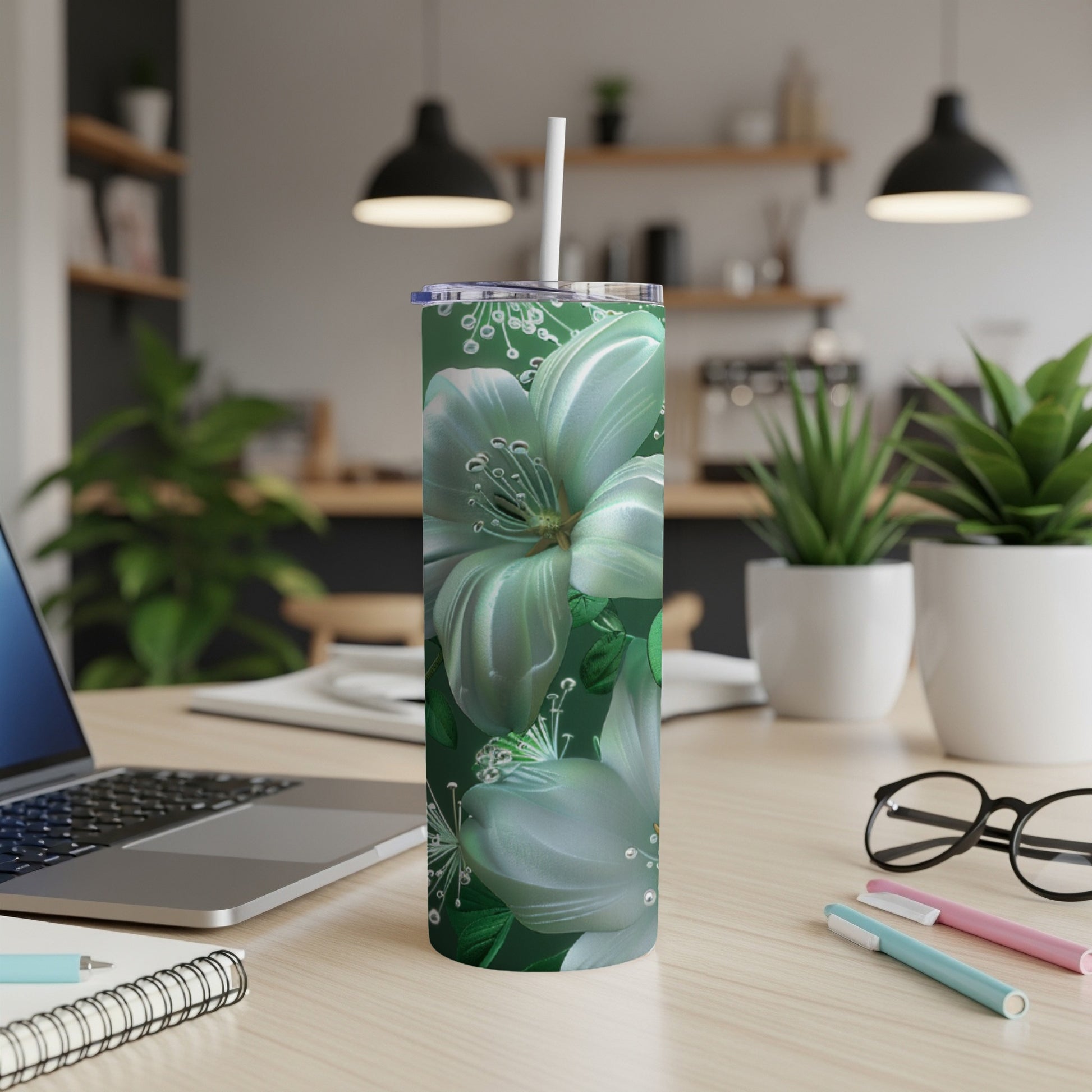 Green floral tumbler with straw on a desk with laptop and pens.