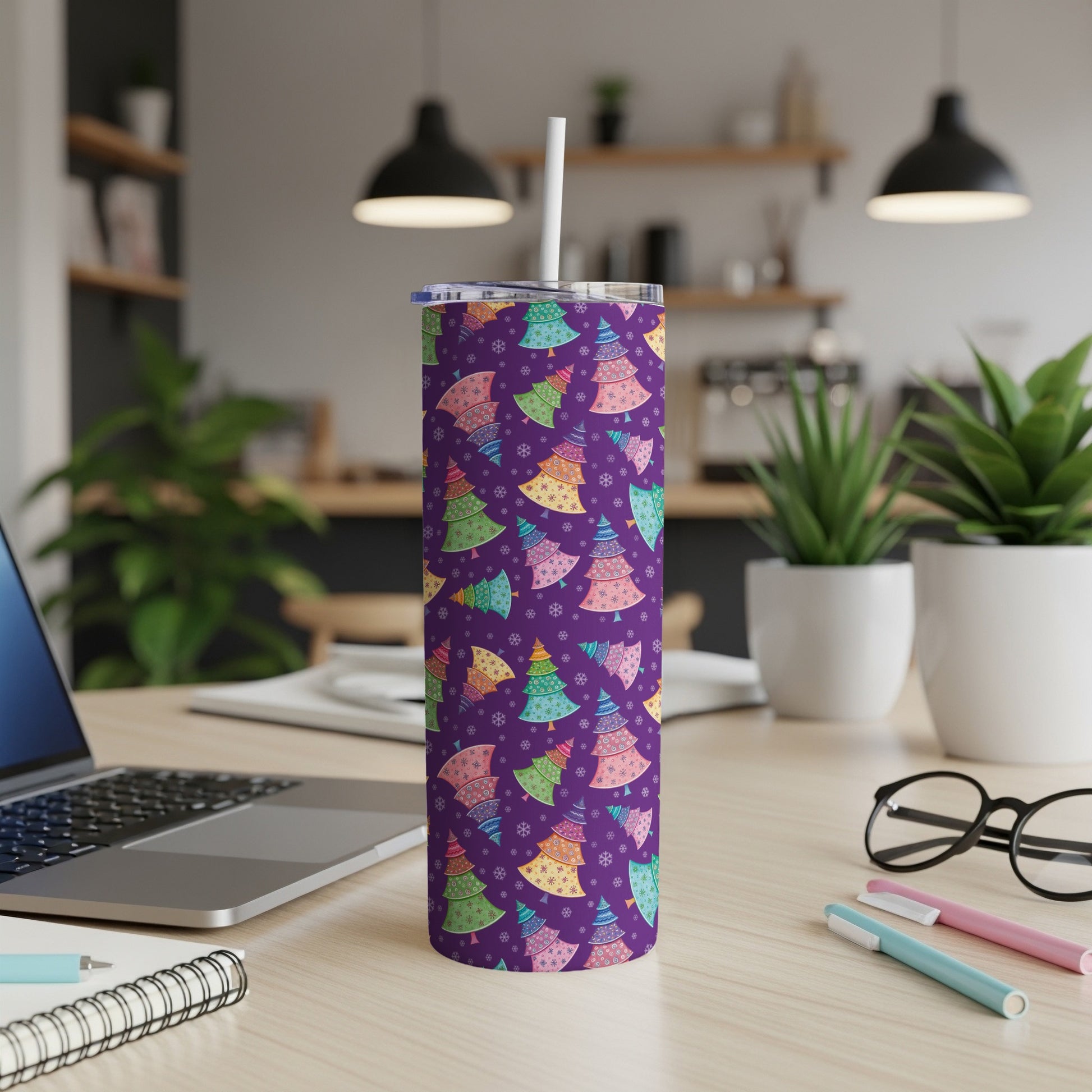 Purple tumbler with colorful Christmas trees and snowflakes, on a desk.