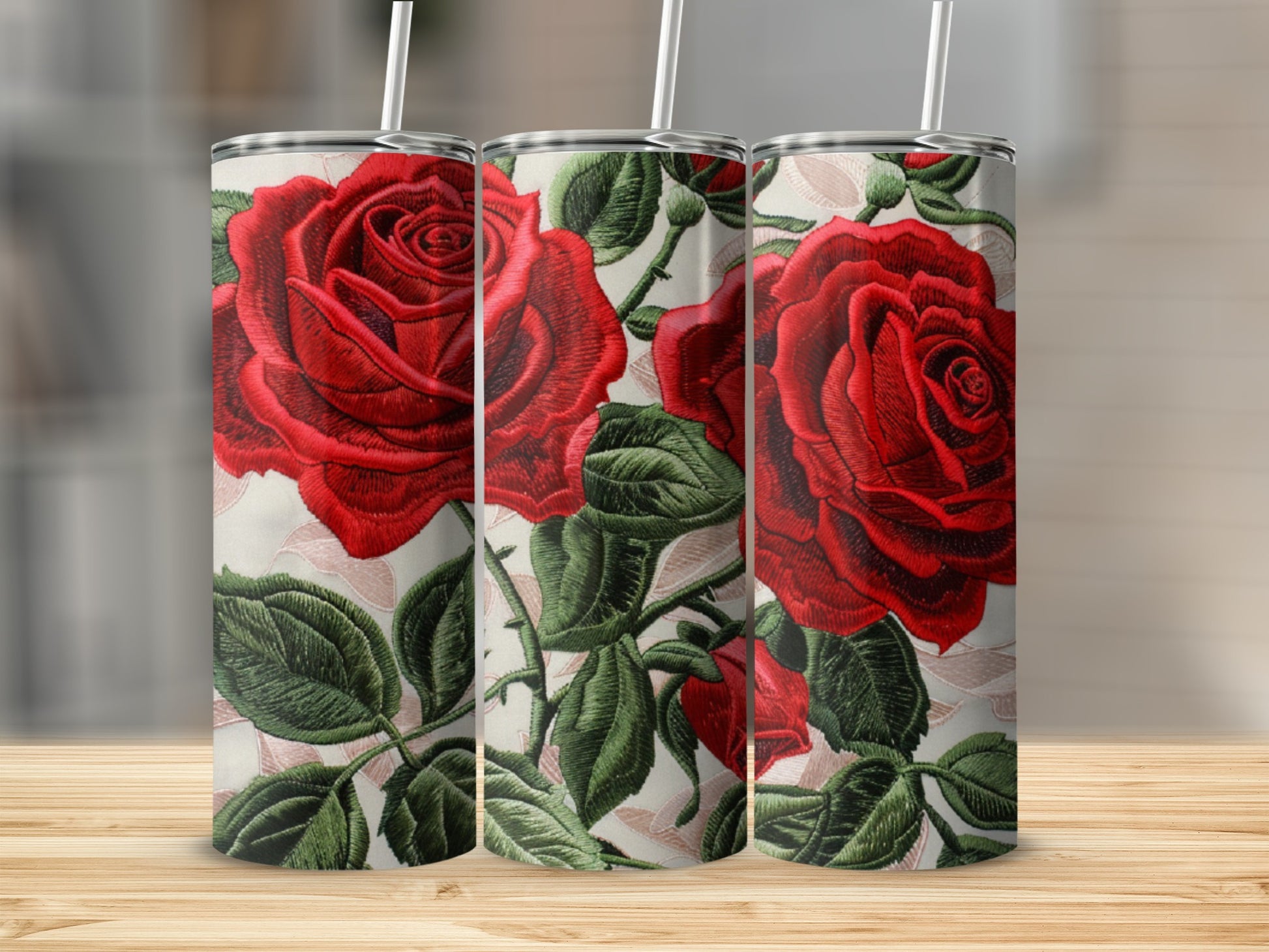 Three tumblers with red roses and green leaves design on a wooden surface.