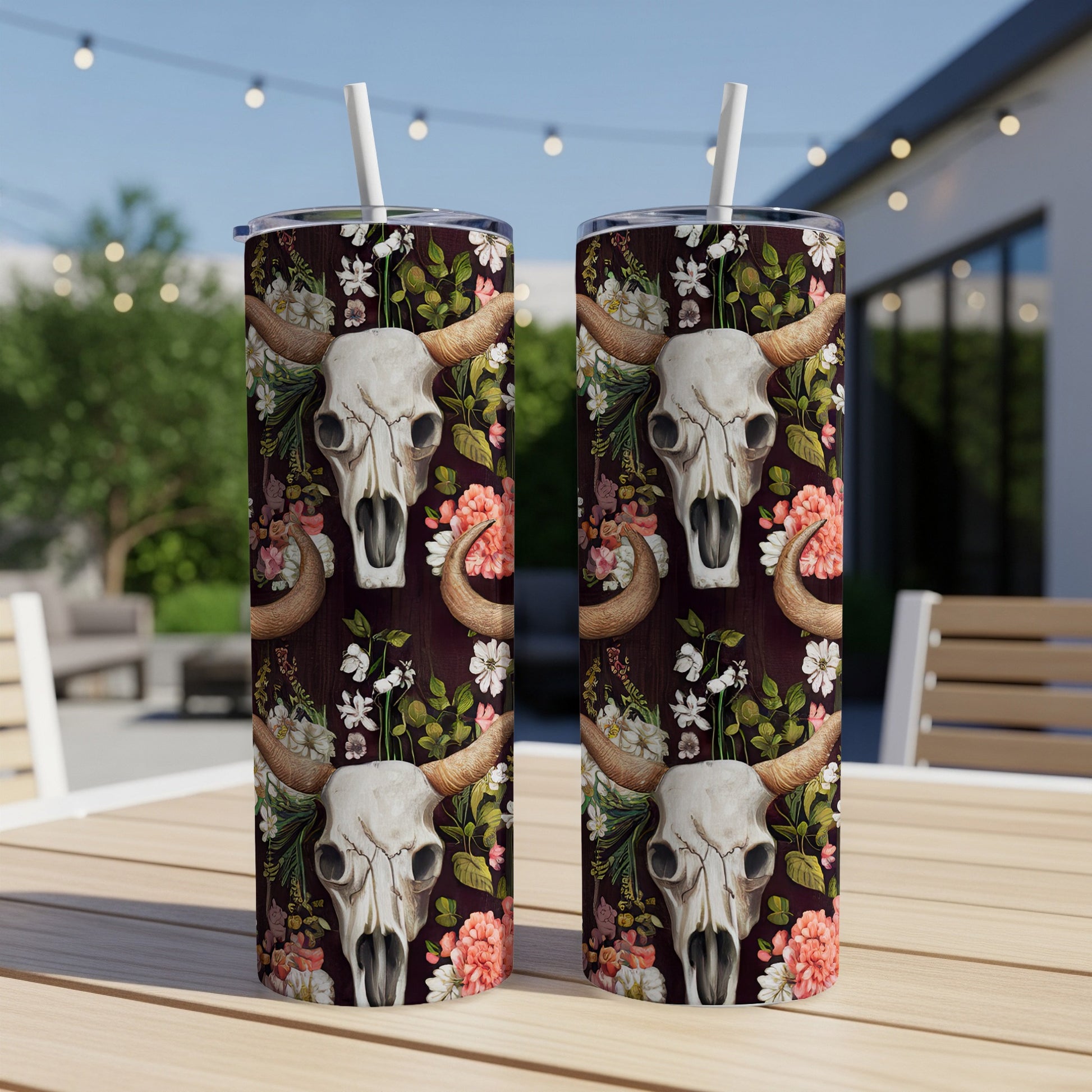 Cow skull and floral pattern on two tumblers with straws on a table.