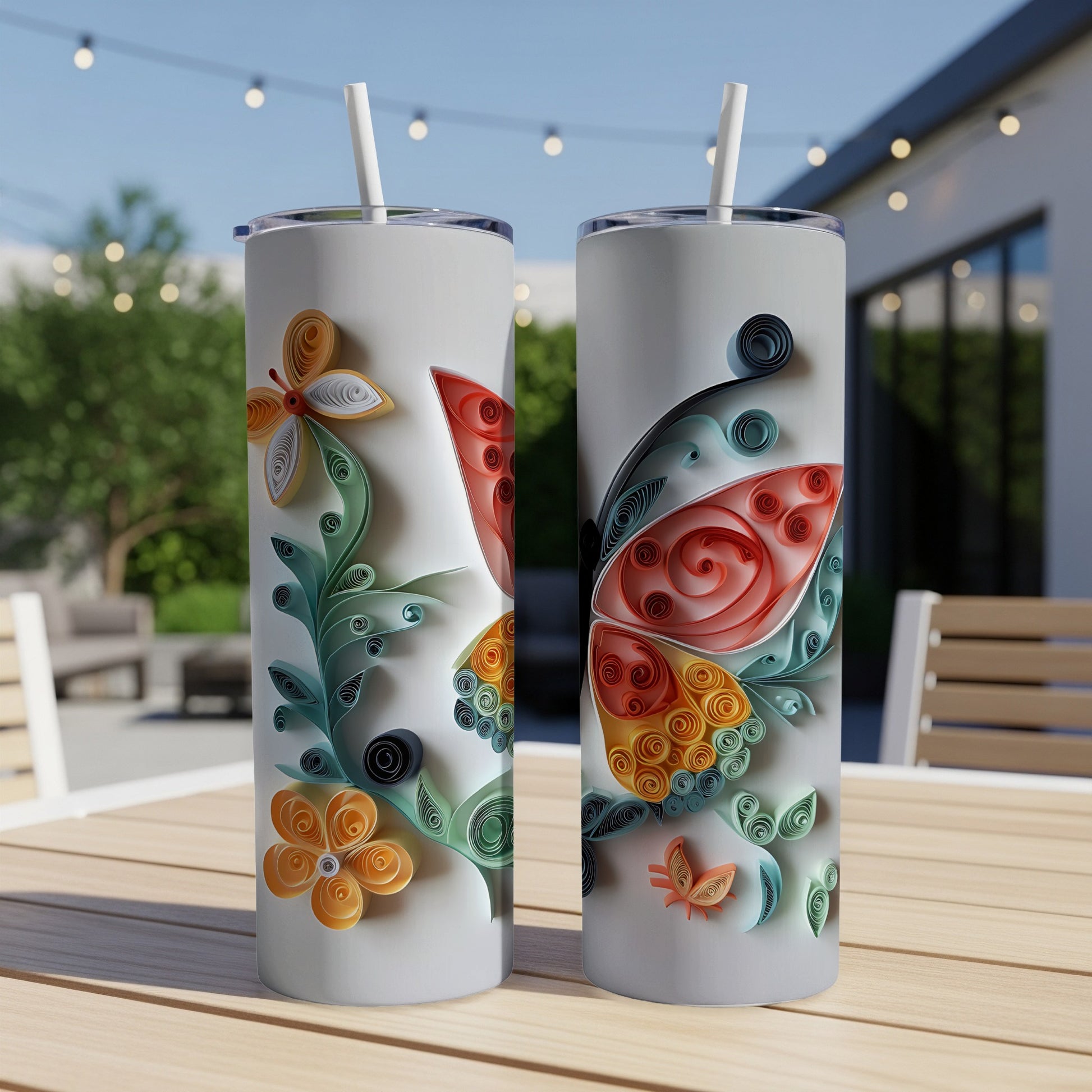Two white tumblers with colorful quilled butterfly and floral designs sit on a wooden table.