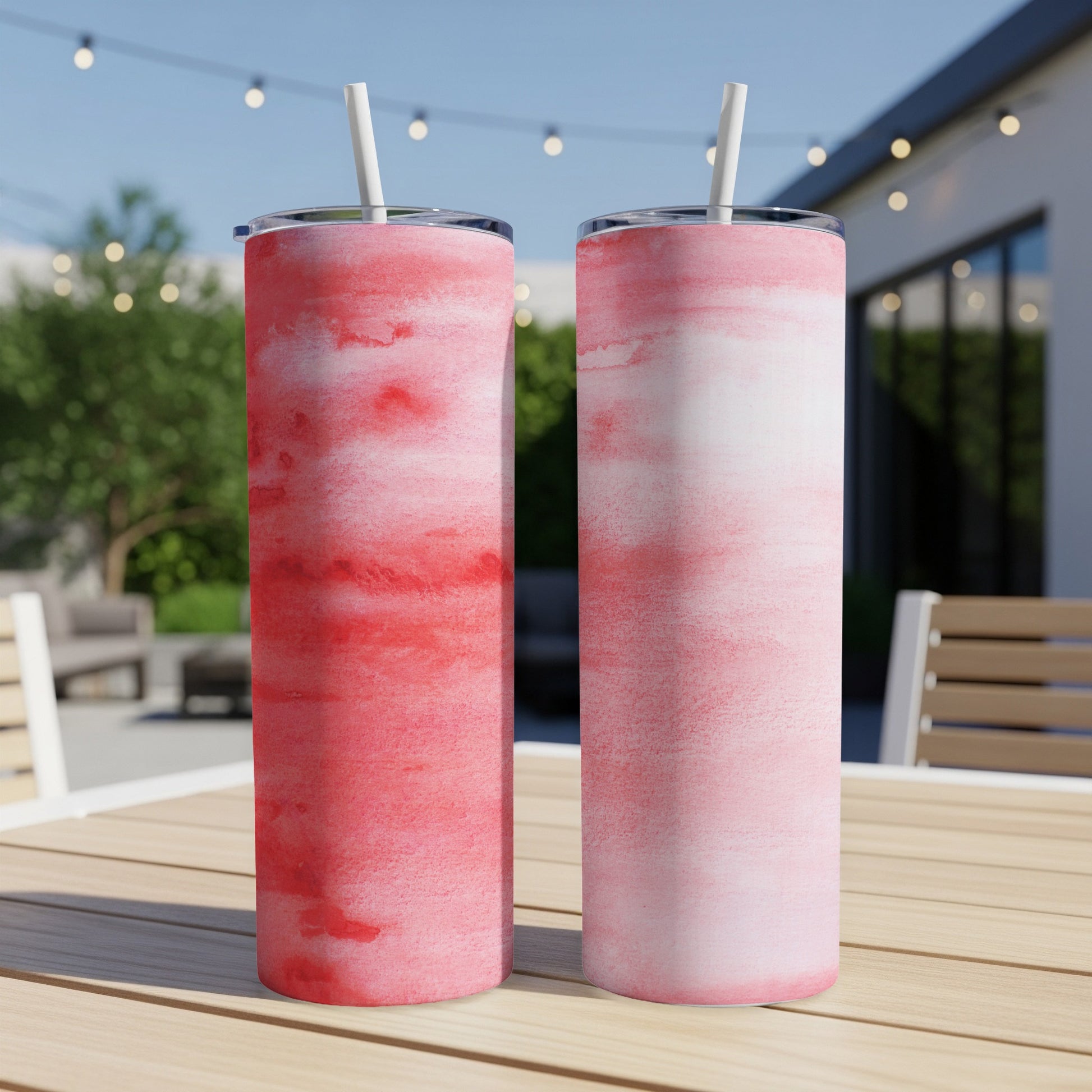 Two tall tumblers with a pink and red watercolor design on a wooden table.