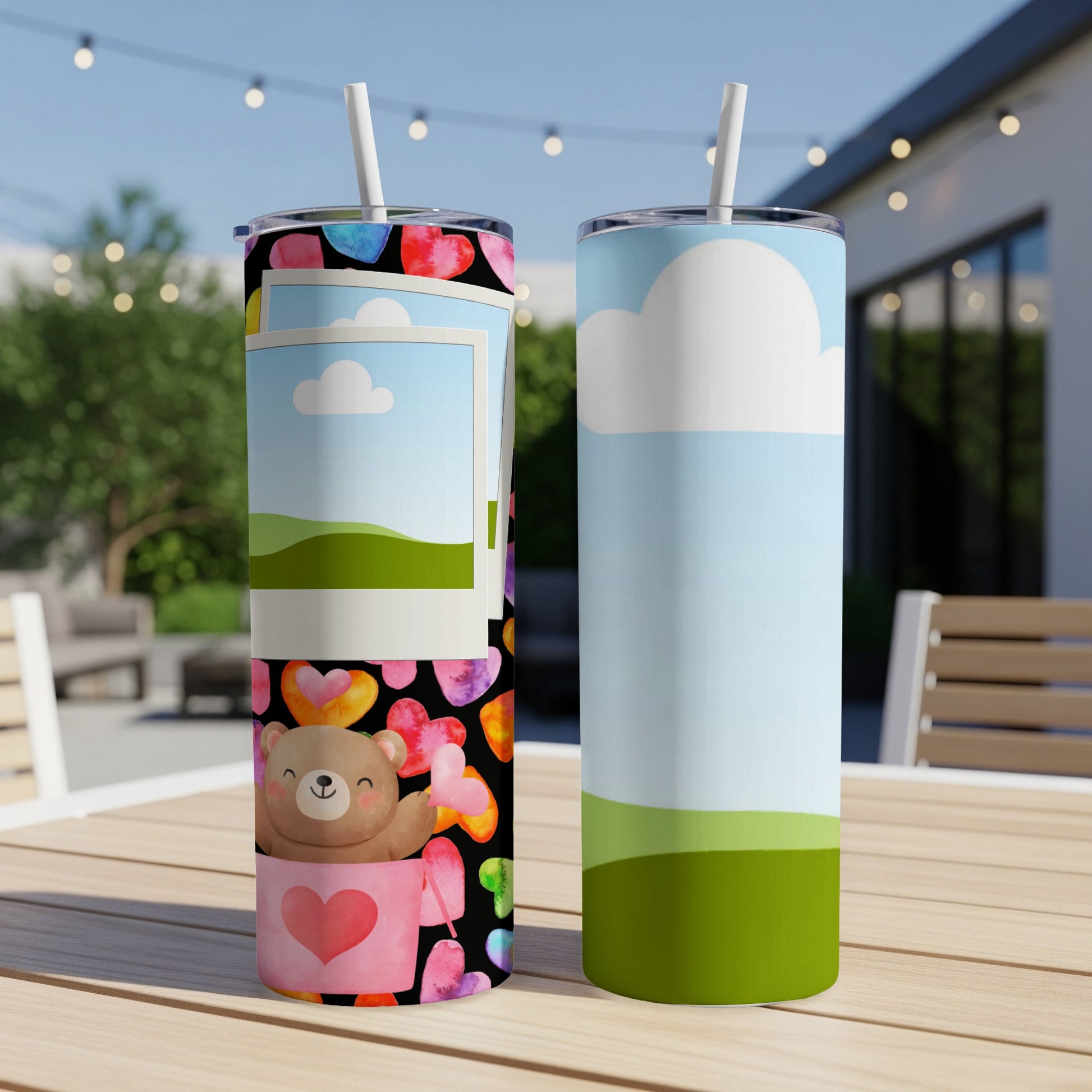 Two tumblers on a wooden table, one with a teddy bear and hearts, the other with a sky and landscape.