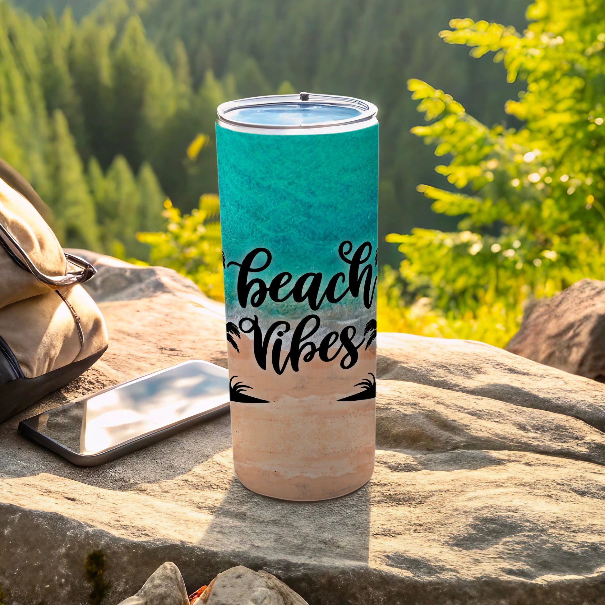 Beach vibes tumbler on rocks with backpack and phone.