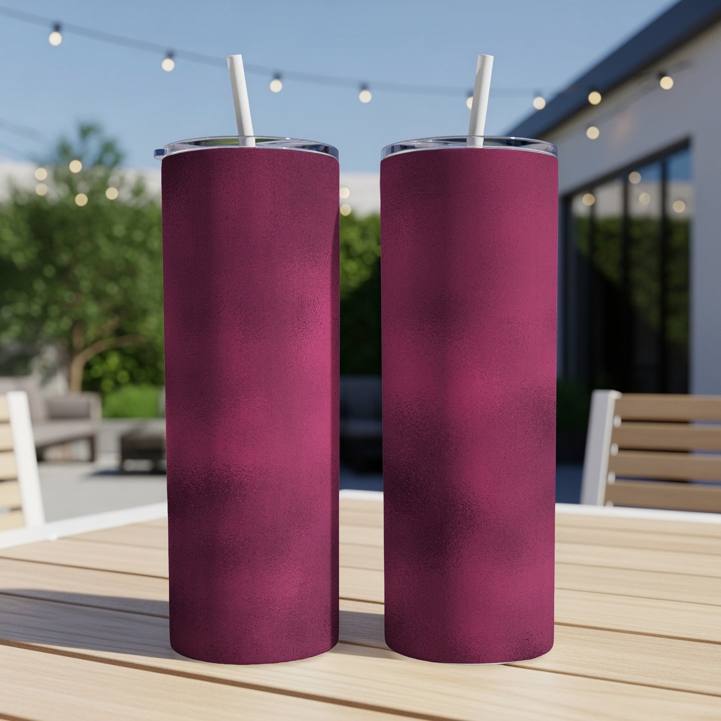 Two matte burgundy tumblers with white straws on a wooden table outdoors.