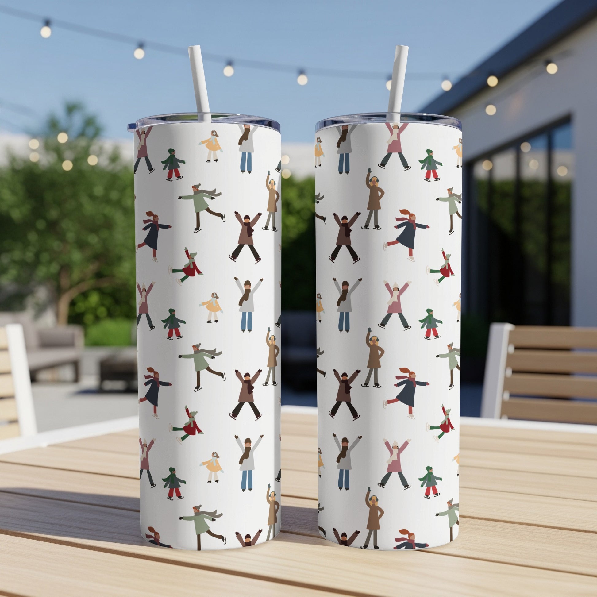Two white tumblers with a pattern of cartoon ice skaters on a table.