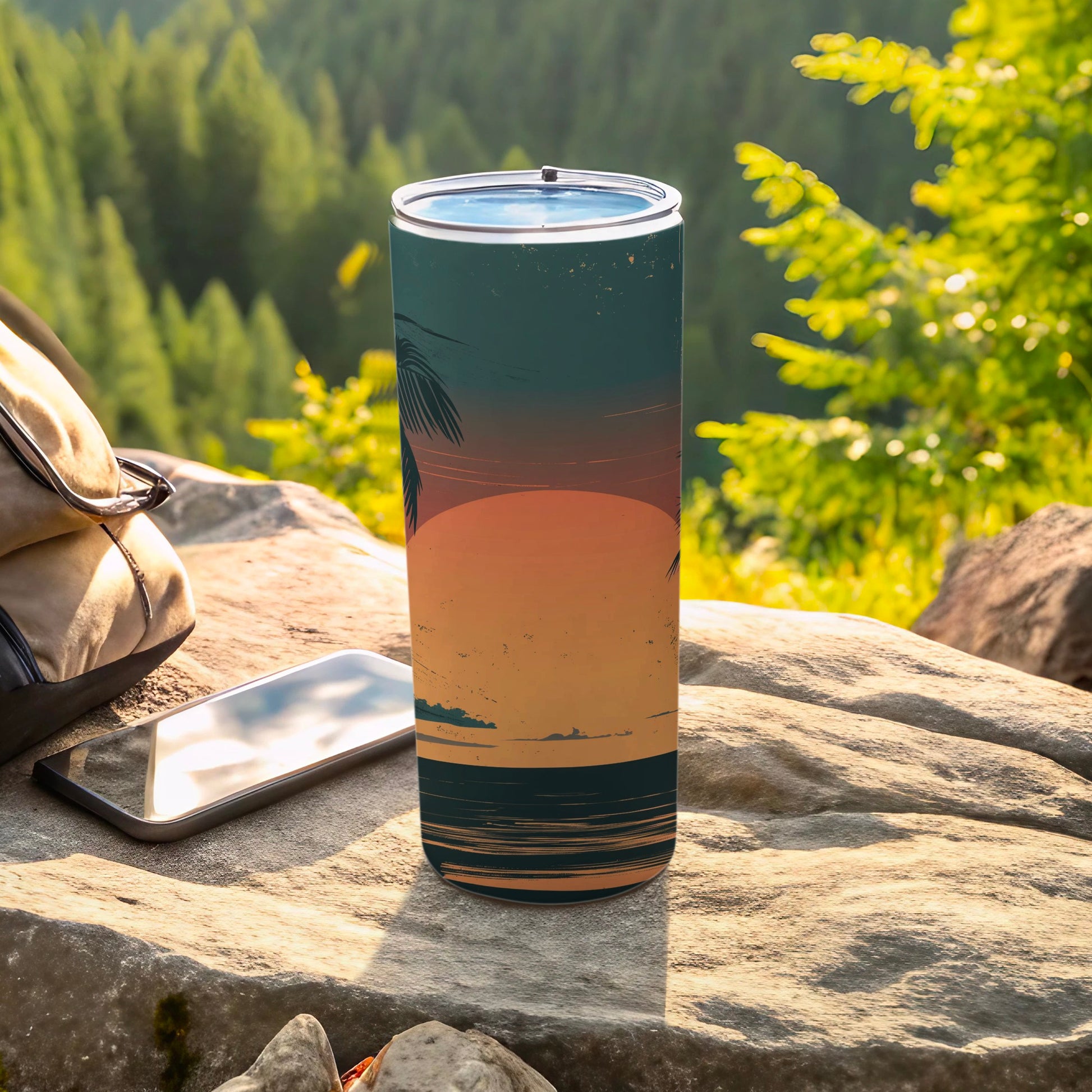 Tall tumbler with a sunset beach design, placed on rocks.