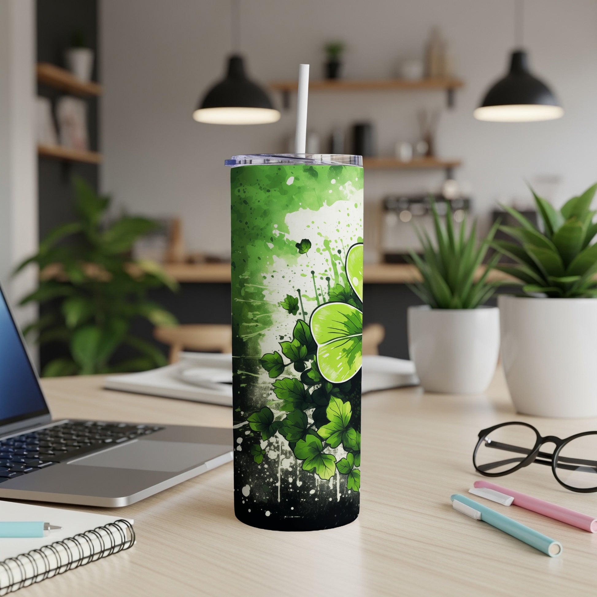 Green shamrock splatter skinny tumbler with straw on desk.
