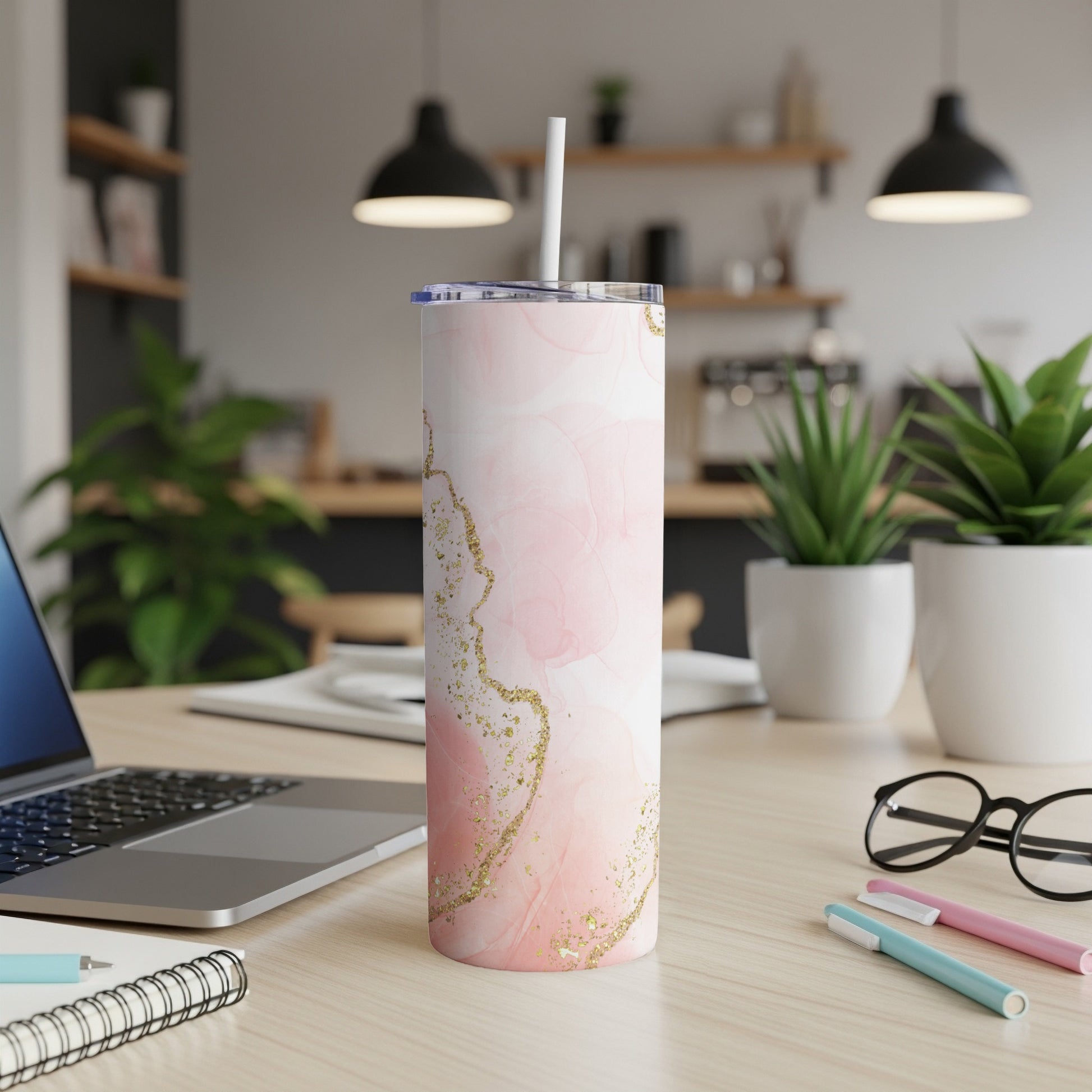 Pink marble and gold glitter tumbler with straw on desk.