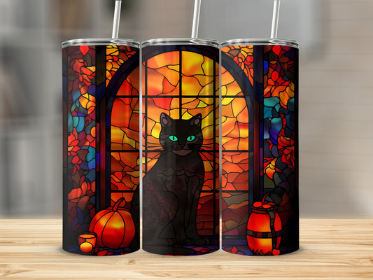 Black cat with green eyes sits in front of a stained-glass window with pumpkins.