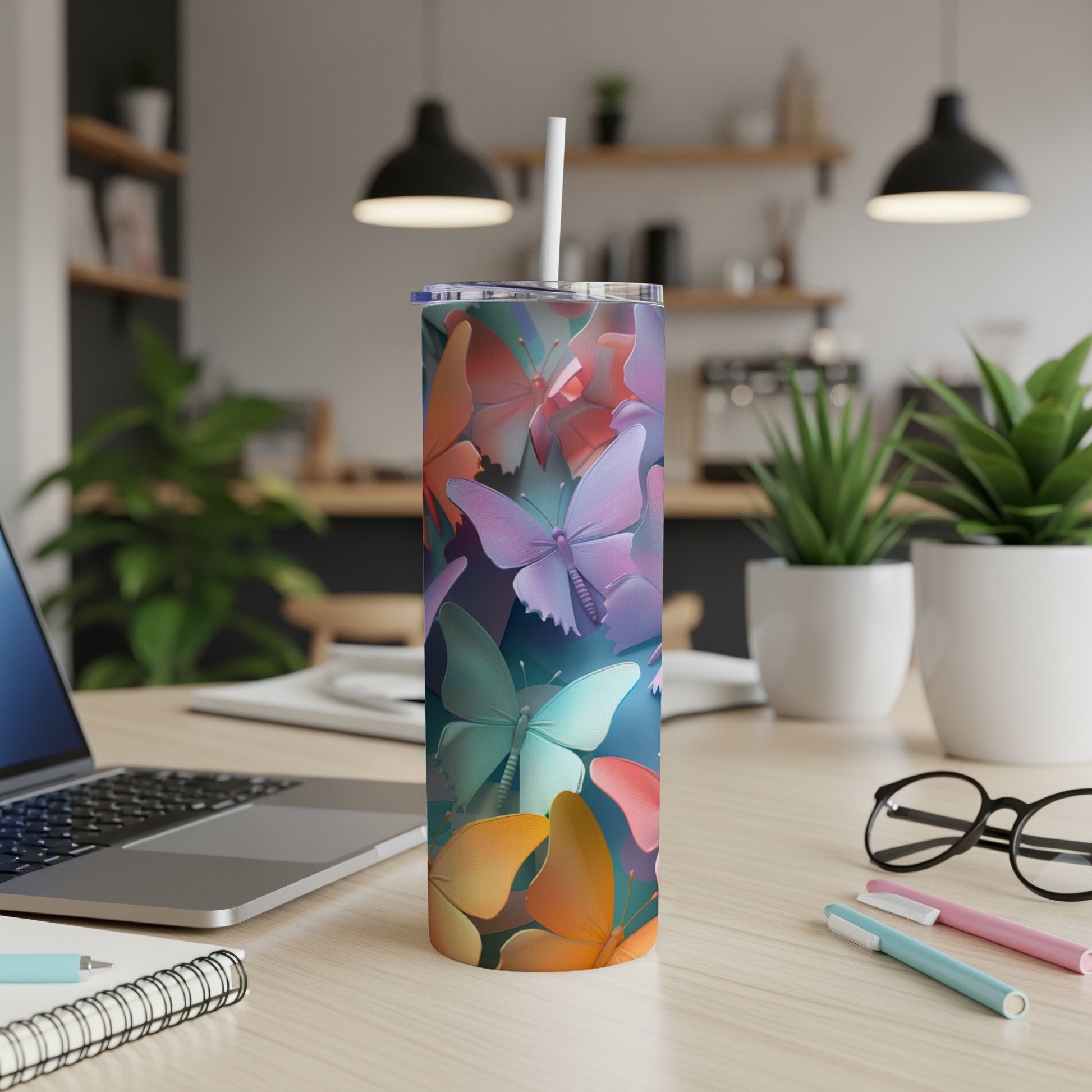 Tumbler with colorful butterflies, laptop, and pens on a desk.