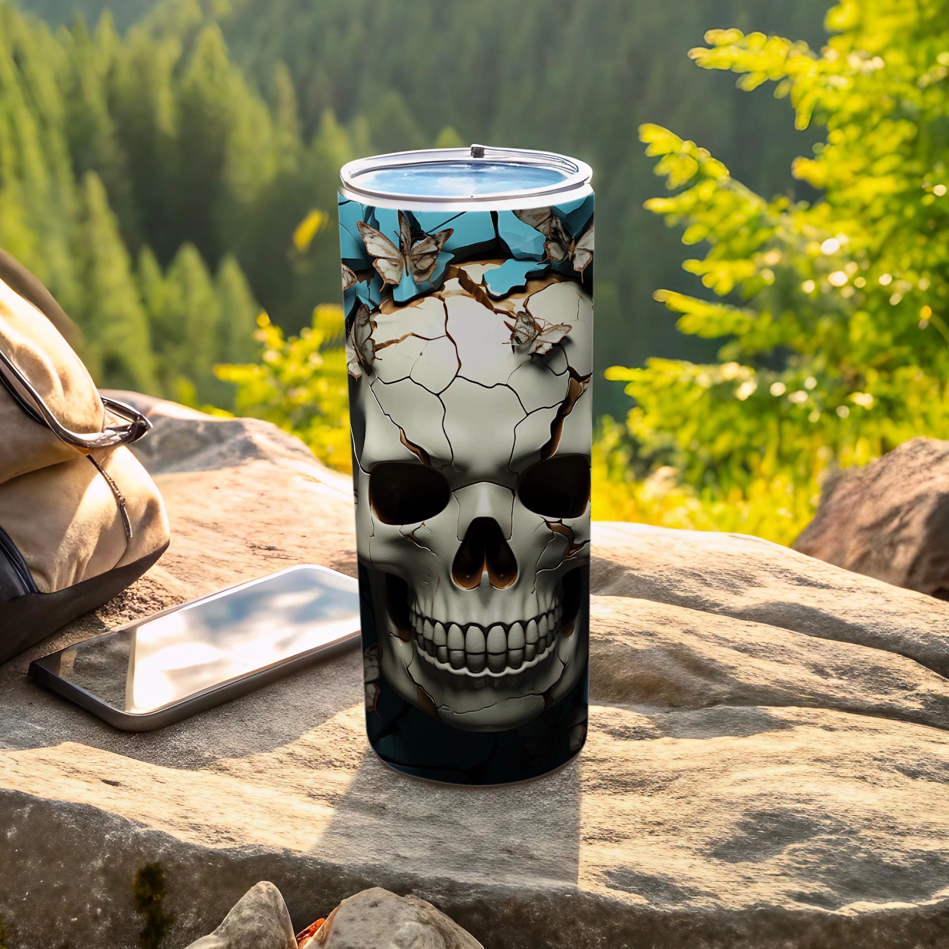 Tumbler with skull and butterfly design on a rock with mountains in background.