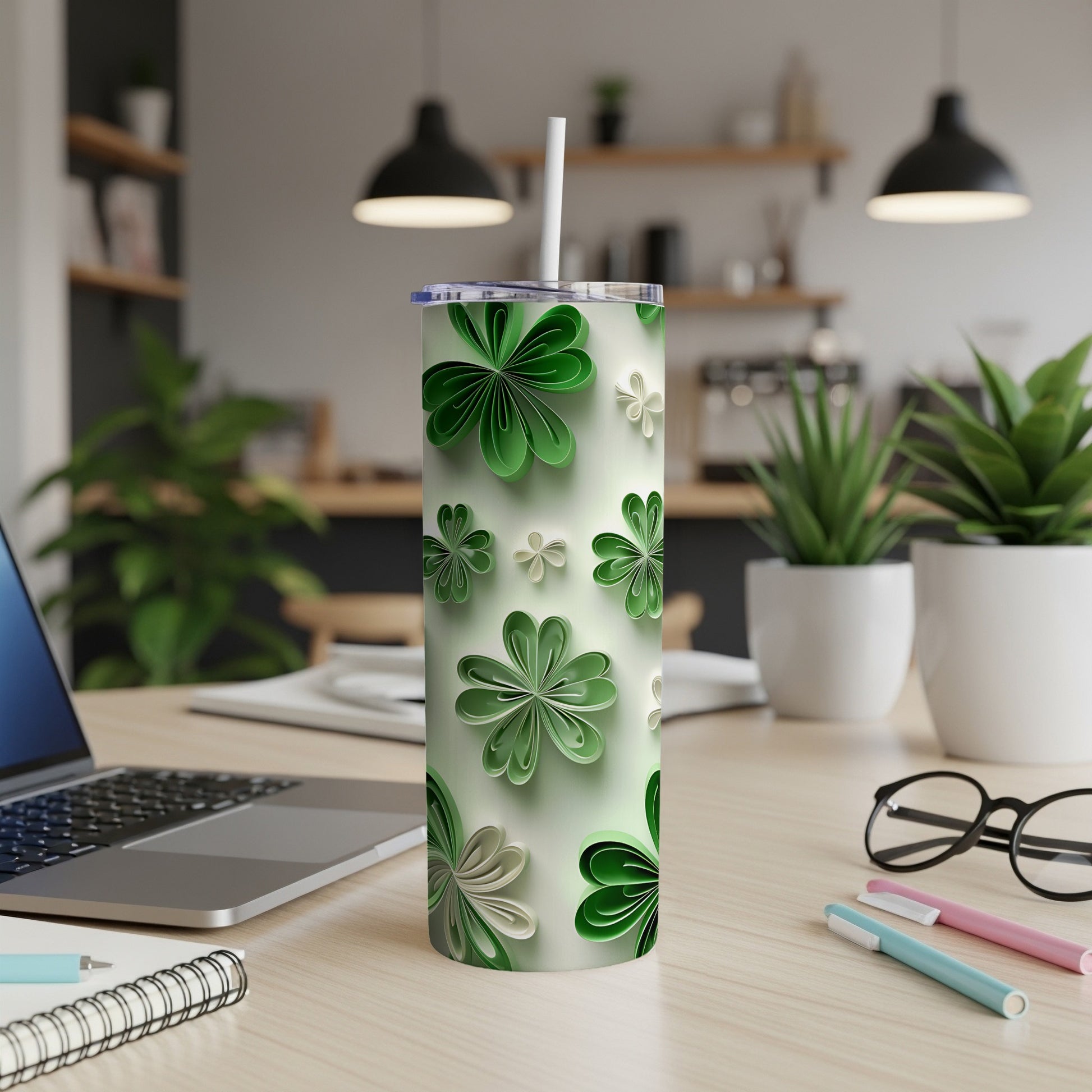 Green floral tumbler with straw on a desk with a laptop and pens.