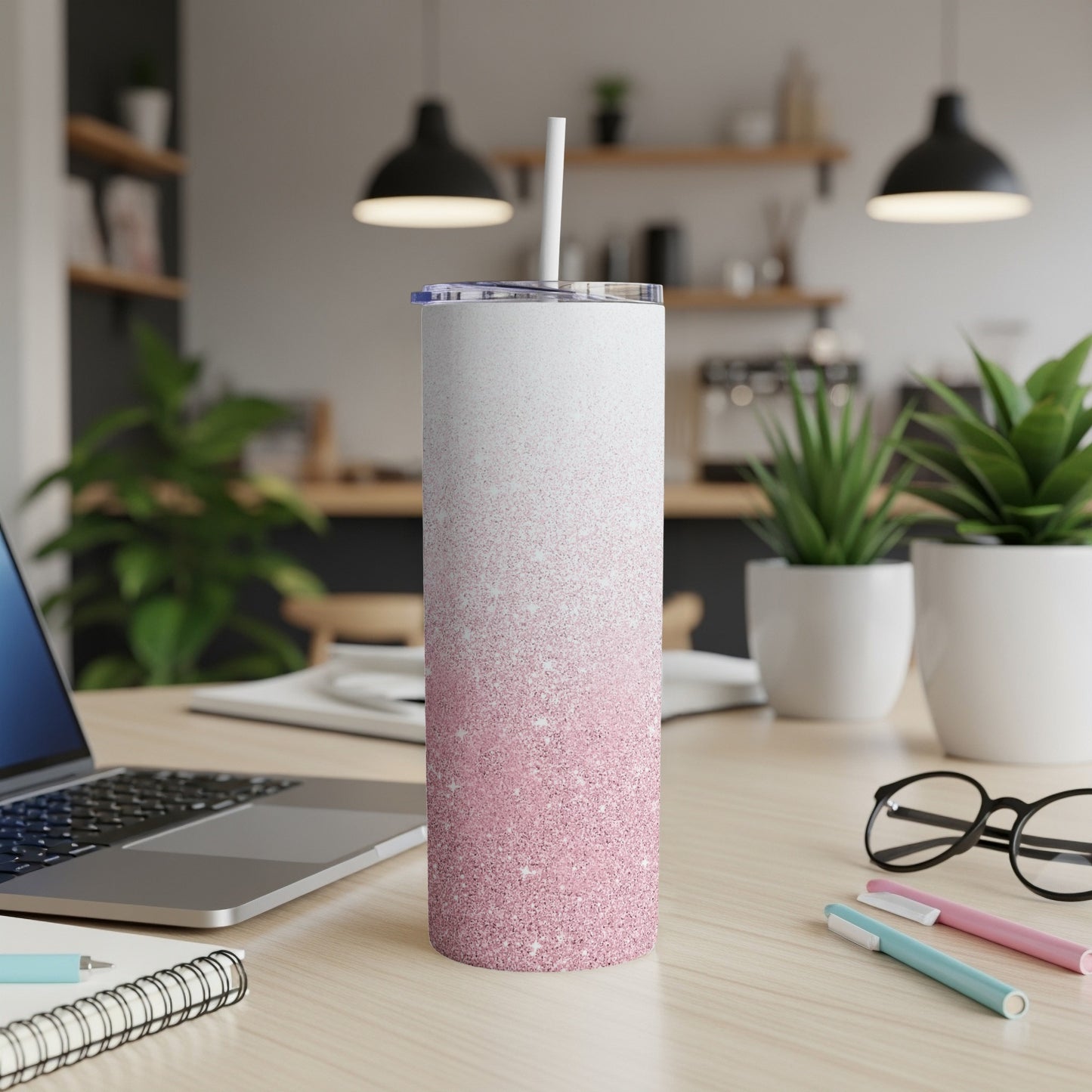 Glitter ombre pink skinny tumbler with straw on desk next to laptop.
