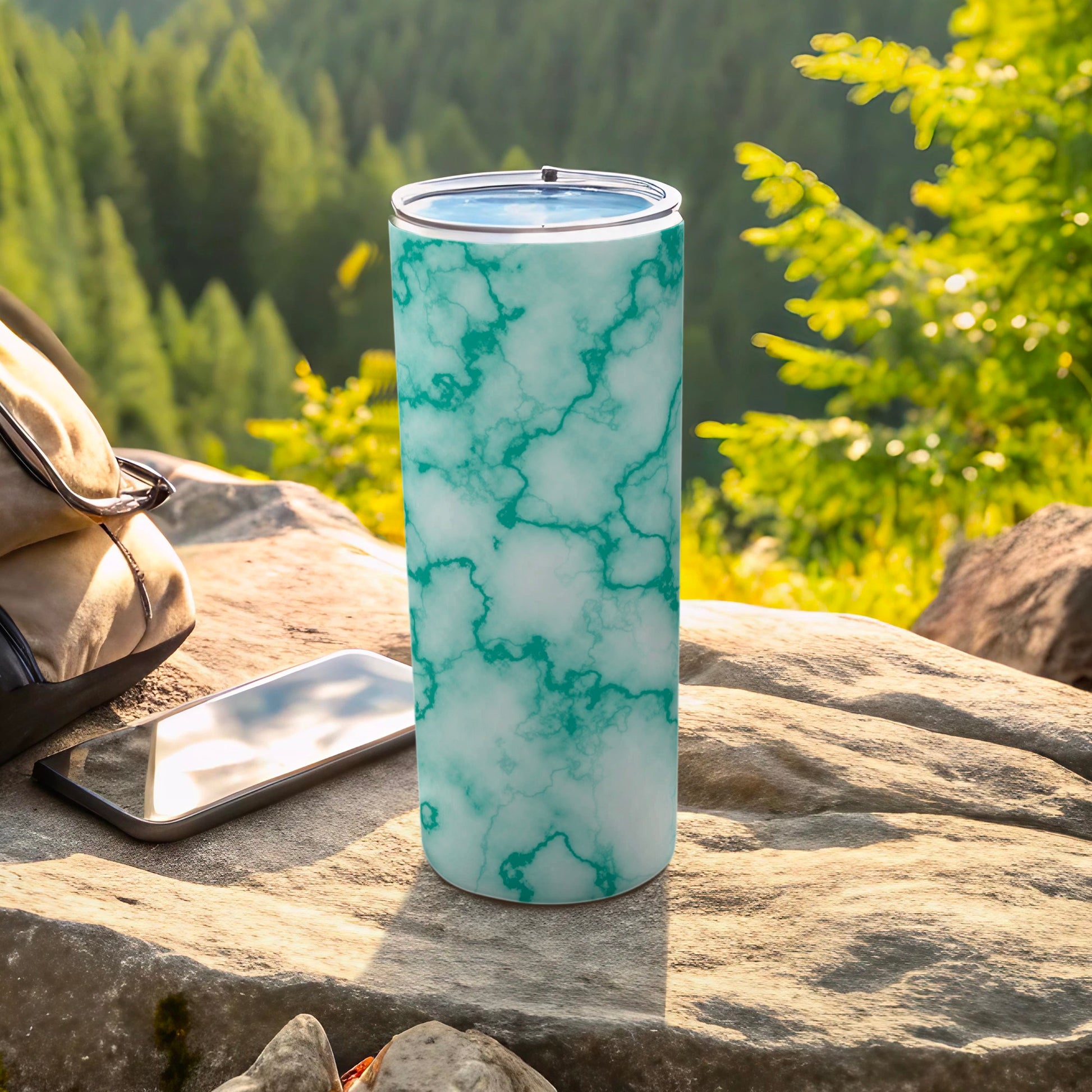 Aqua marble pattern tumbler with straw, next to phone and backpack.