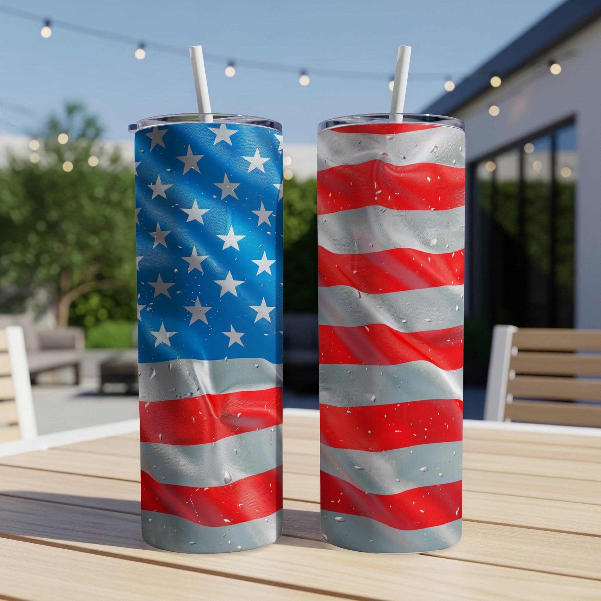 Two tumblers with American flag designs stand on a wooden table outdoors.