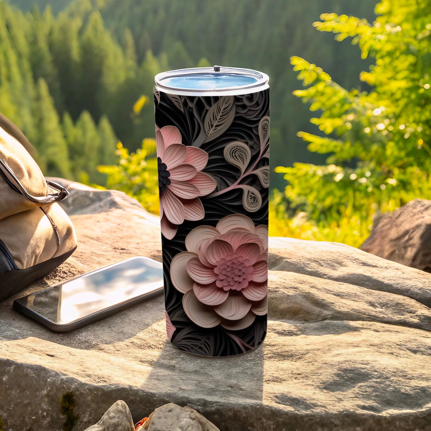 Black tumbler with pink and beige floral design on a rocky surface.