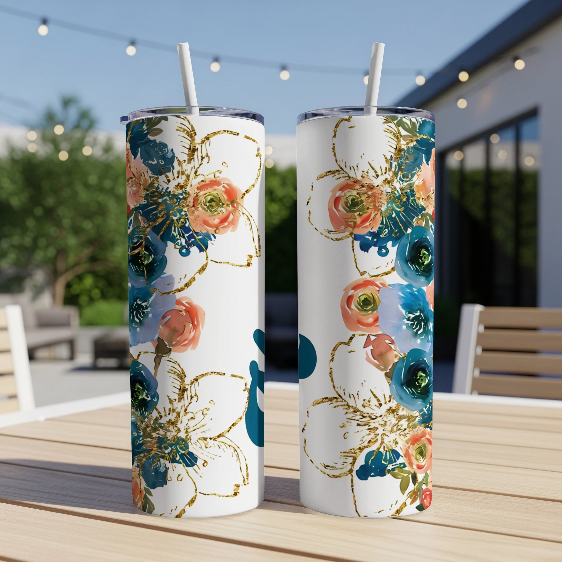 Two white tumblers with floral designs and straws on a wooden table.