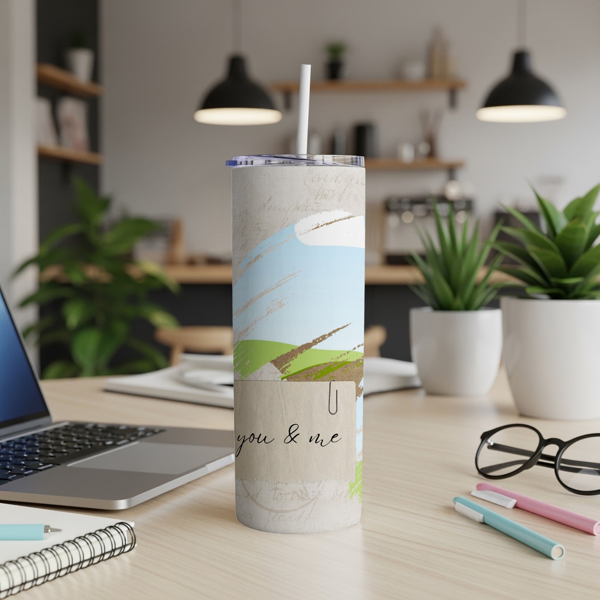 Tumbler with "you & me" text and abstract landscape design on a desk.