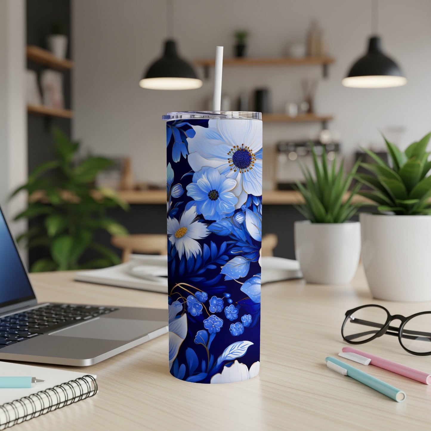 Blue floral tumbler with straw on desk next to laptop and pens.