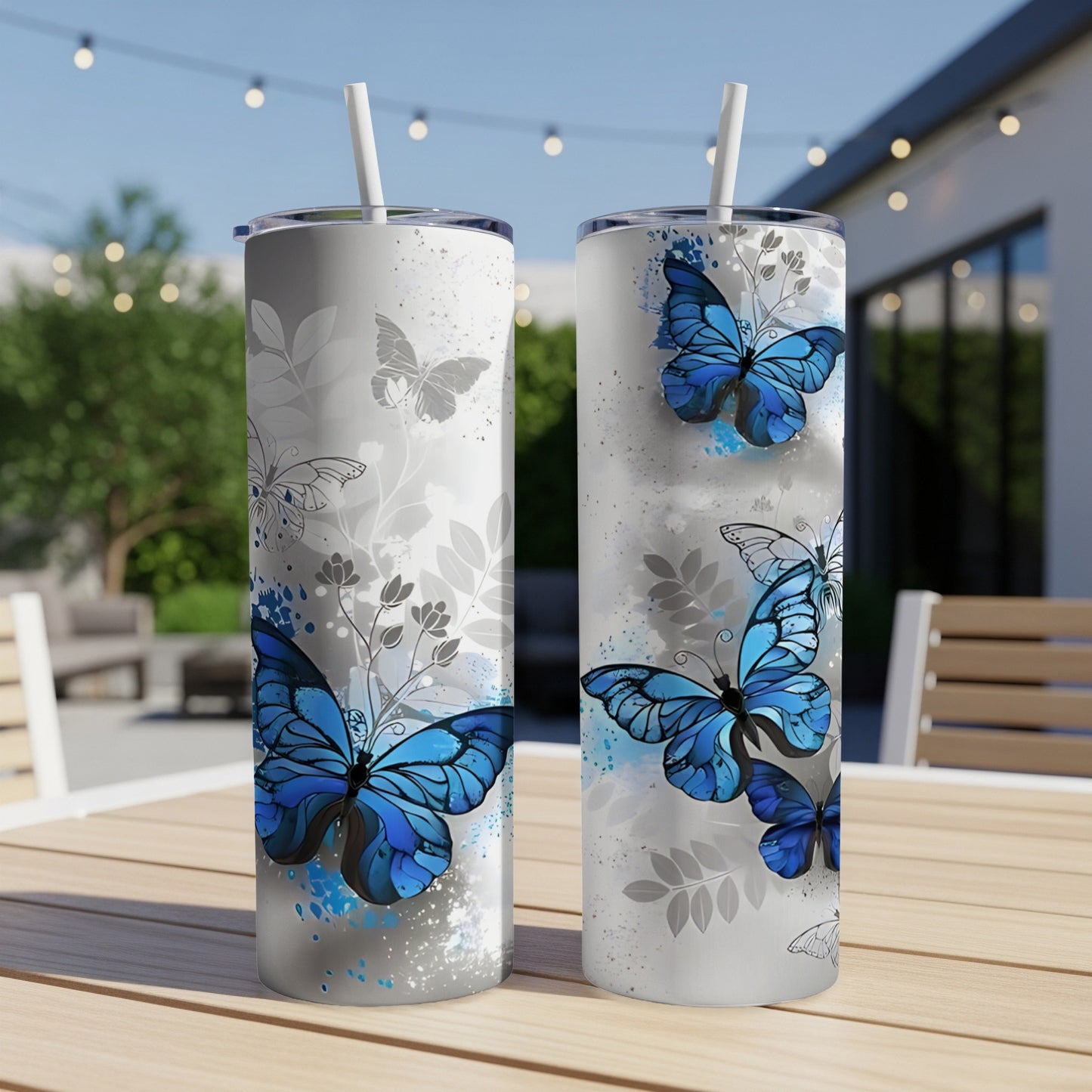 Two tumblers with blue butterflies and grey floral patterns on a patio table.