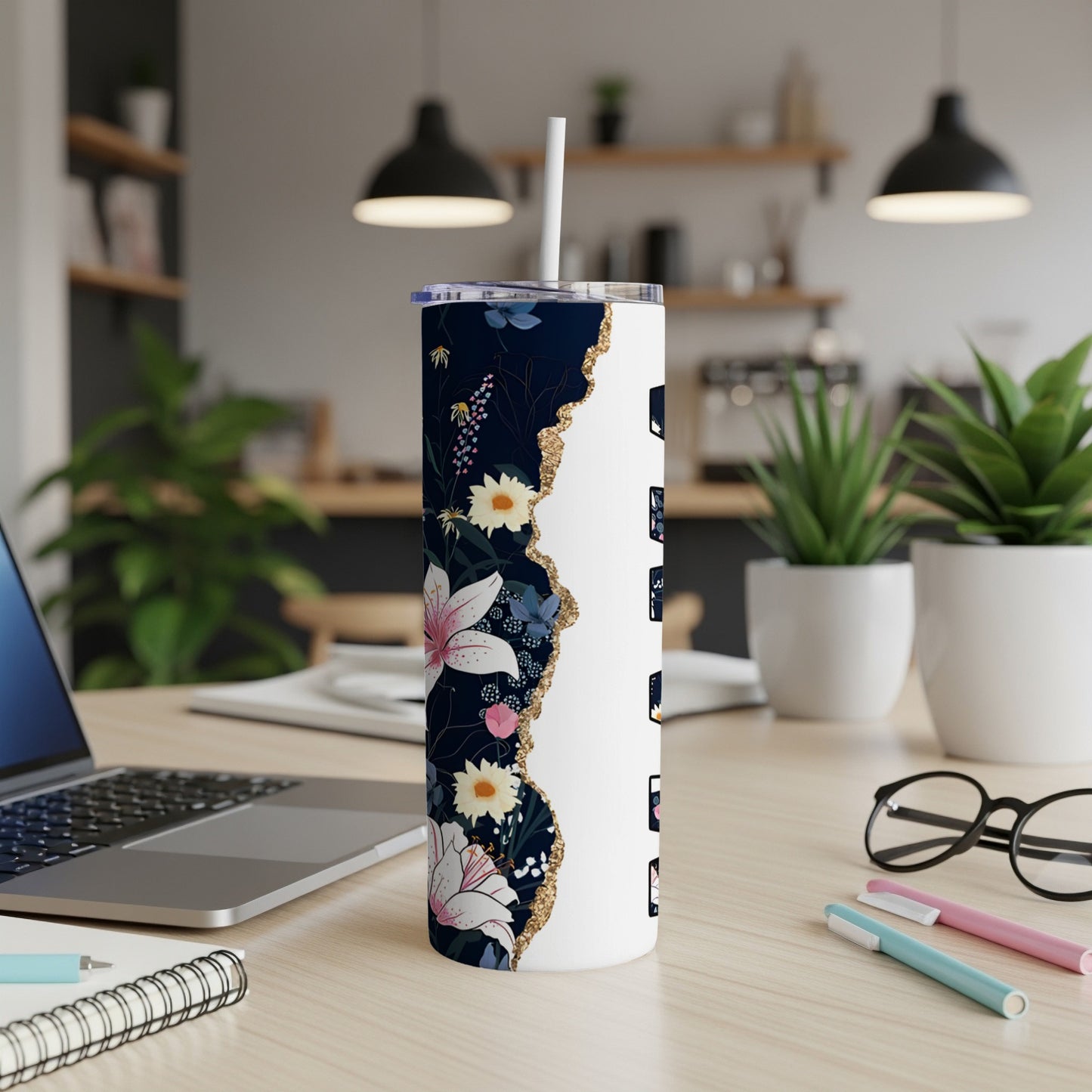 Floral tumbler with white lid and straw on desk next to laptop and pens.