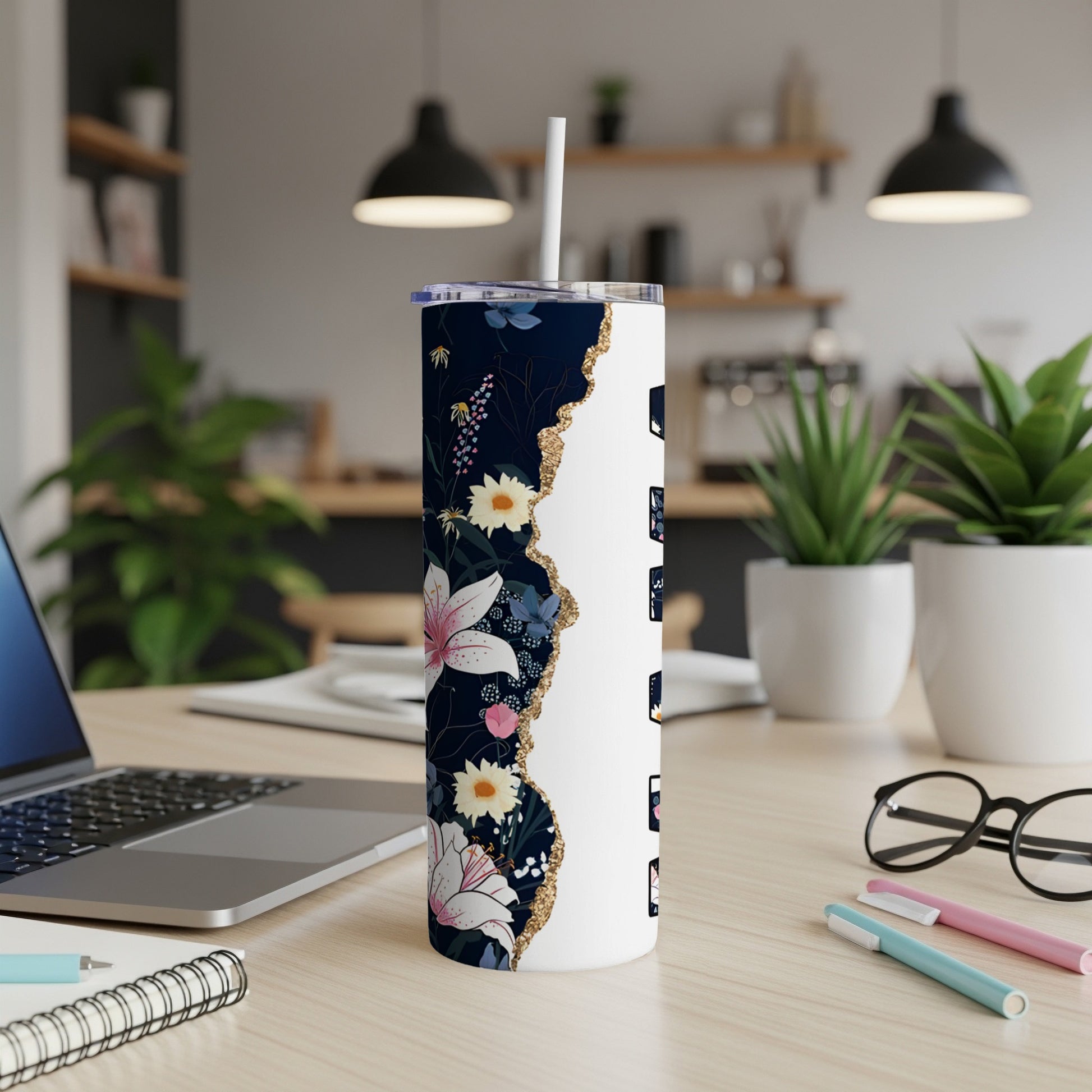 Floral tumbler with white lid and straw on desk next to laptop and pens.