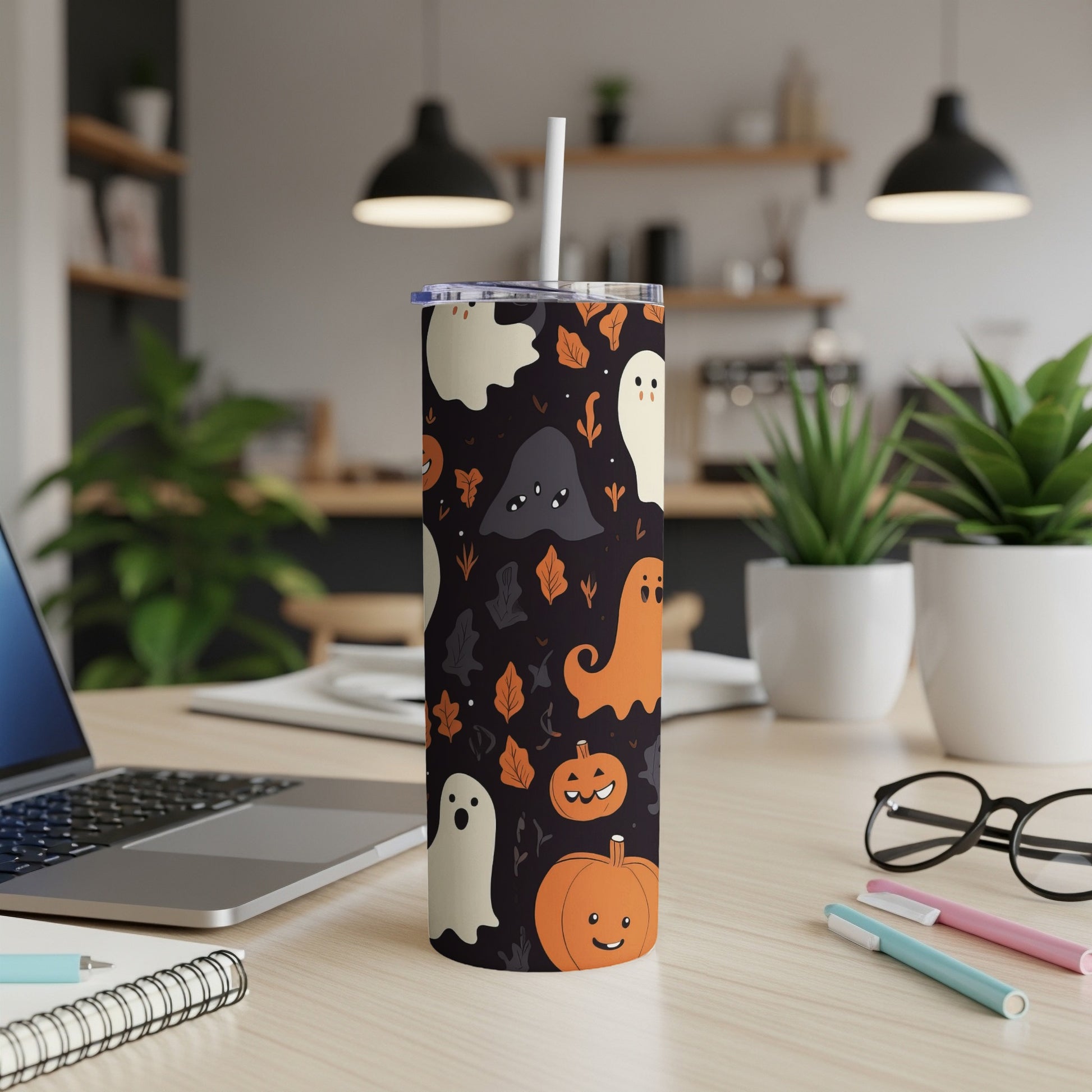 Tumbler with Halloween ghosts and pumpkins pattern on a desk.