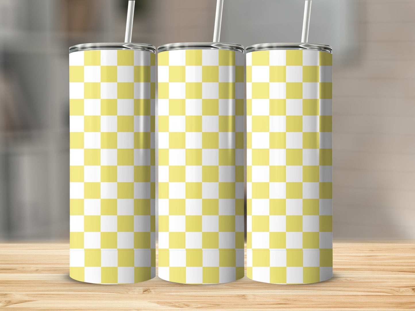 Three yellow and white checkered tumblers with straws on a wooden surface.